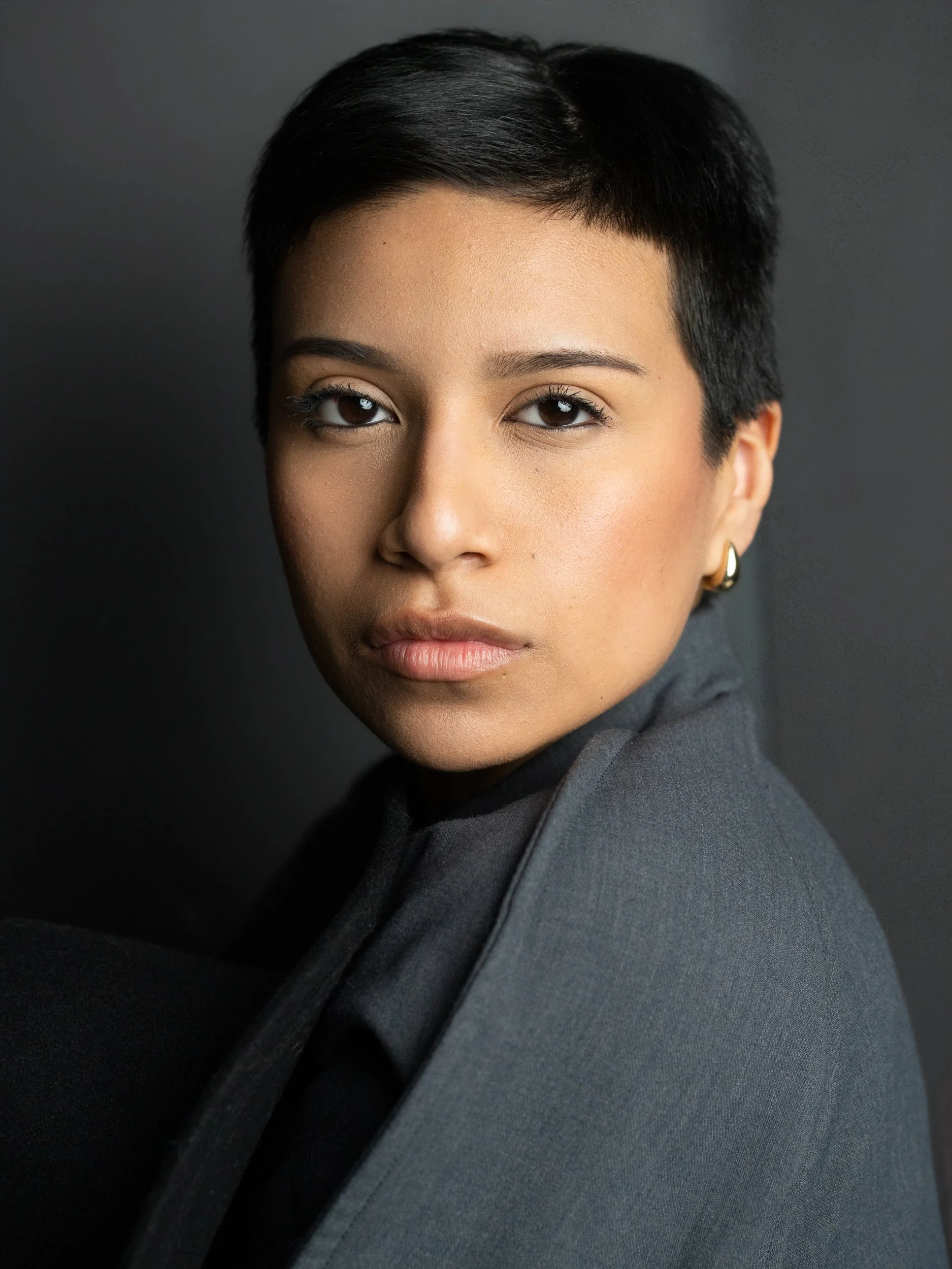 Amanda, portrait session at 9 Studios, SoHo NYC — close editorial portrait, slate blazer over black turtleneck, three-quarter turn, steady gaze, dark gray background, May 2026