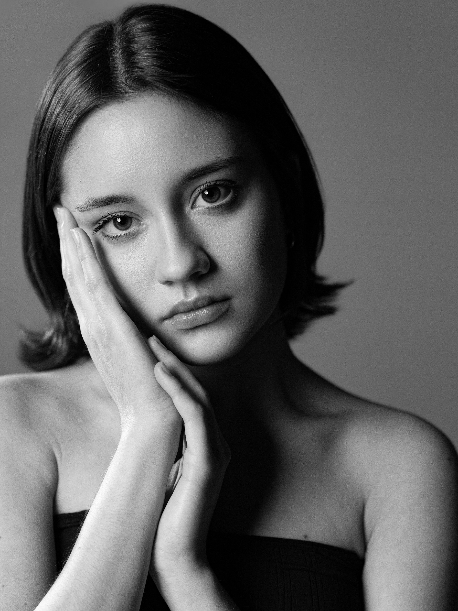 Yasmin, black and white portrait with hands pressed to cheek, contemplative expression, short dark bob, bare shoulders, studio