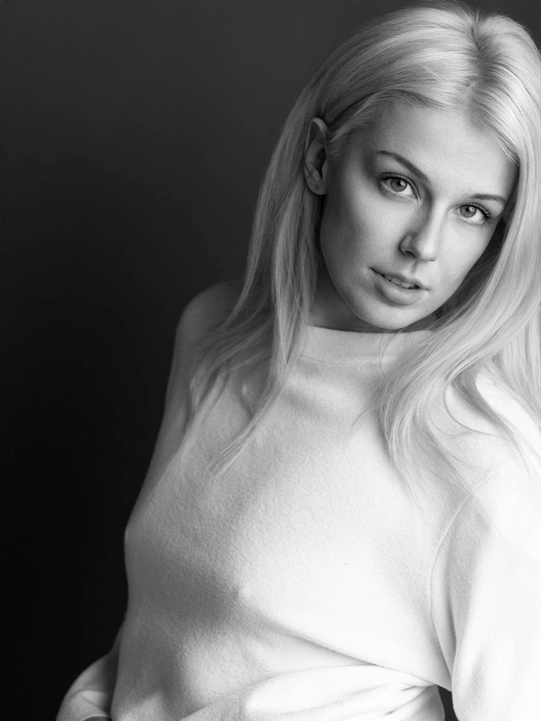 Lianna, black and white portrait with direct gaze, long platinum hair, white plush sweater, dark studio background