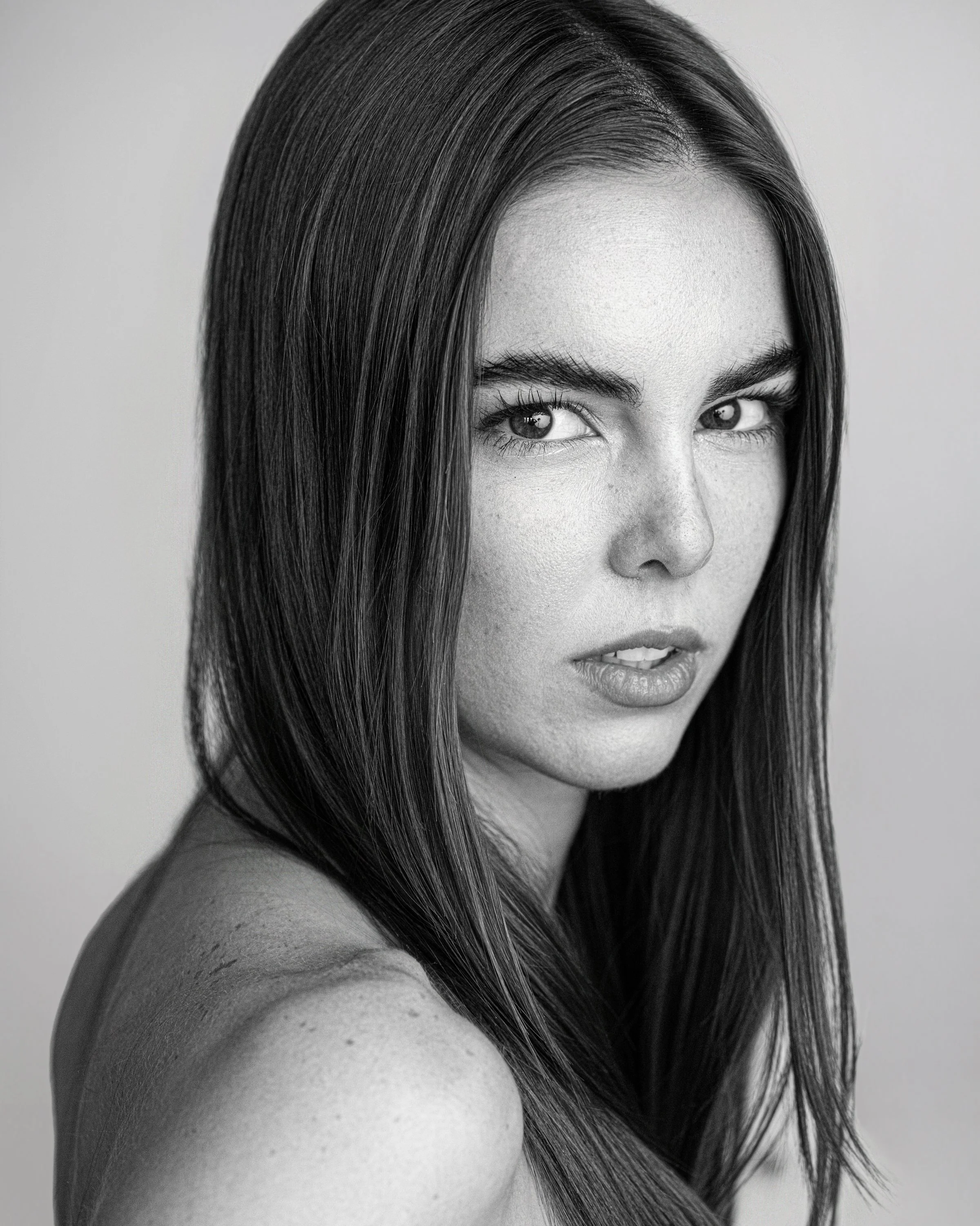 Shannon, black and white portrait looking over shoulder with intense gaze, straight dark hair, freckles, studio