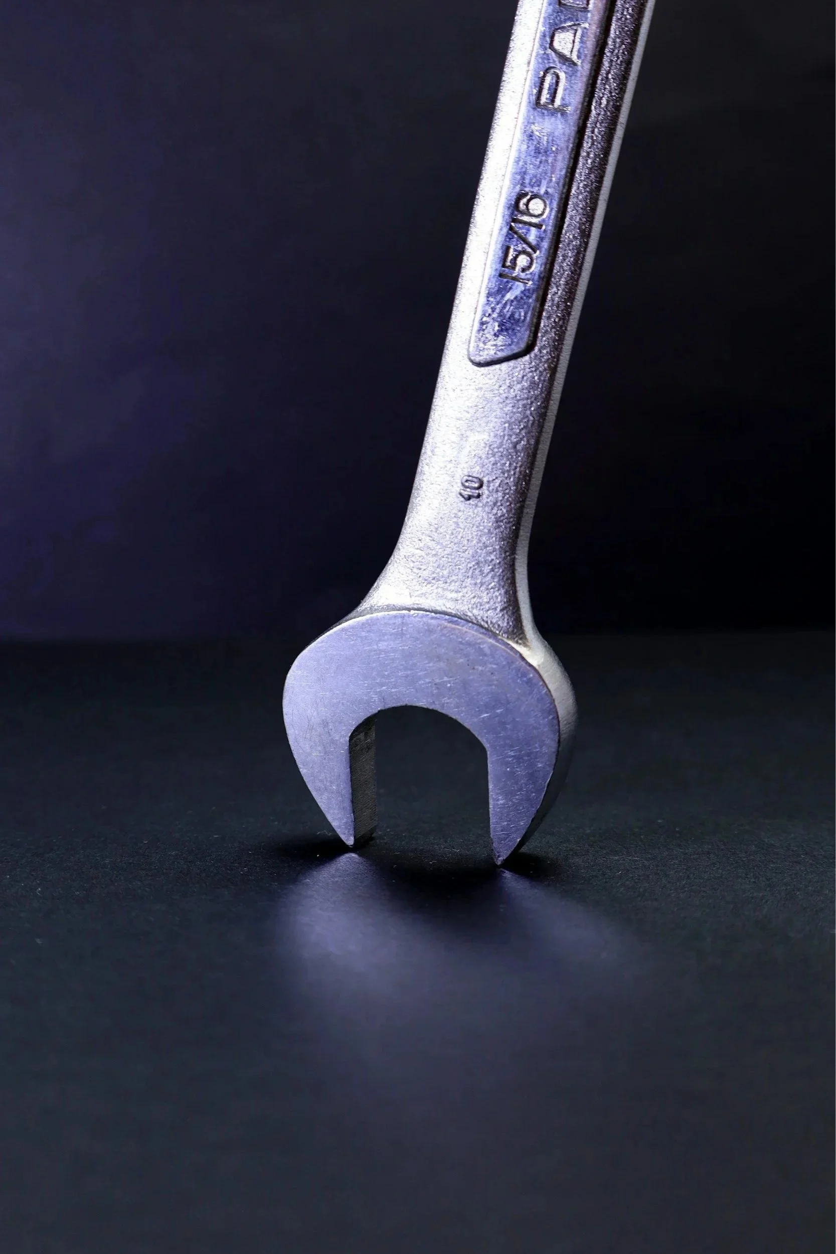 Close-up of a small open-end wrench on a black surface with a dark background.