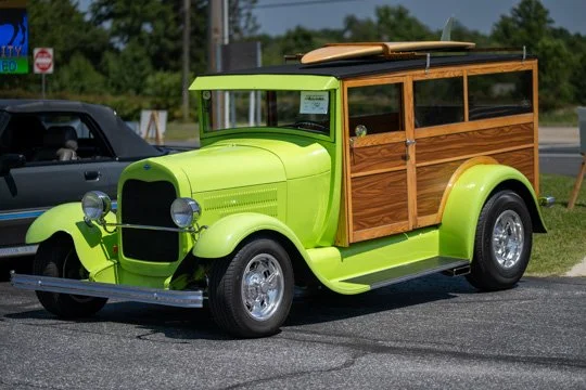 A vintage lime green car with wooden paneling on the sides and a roof rack, parked on a road.