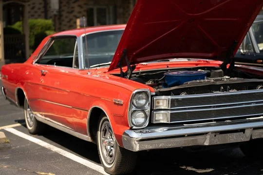A red vintage car with its hood open, parked in a parking lot.