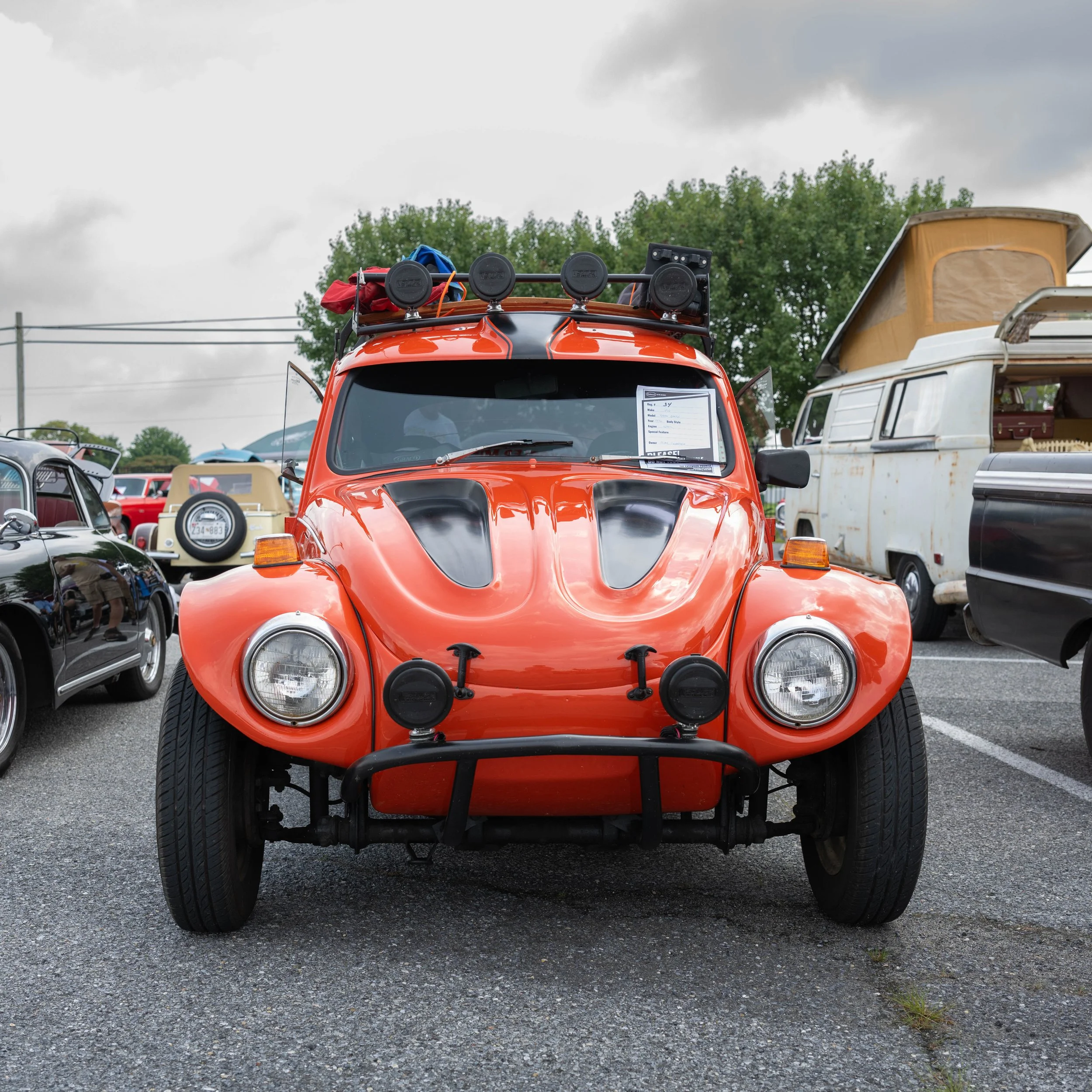 Front view of a vintage red amphibious car with black fender flares, round headlights, and lights on the front and roof, parked among other classic vehicles on an outdoor lot.