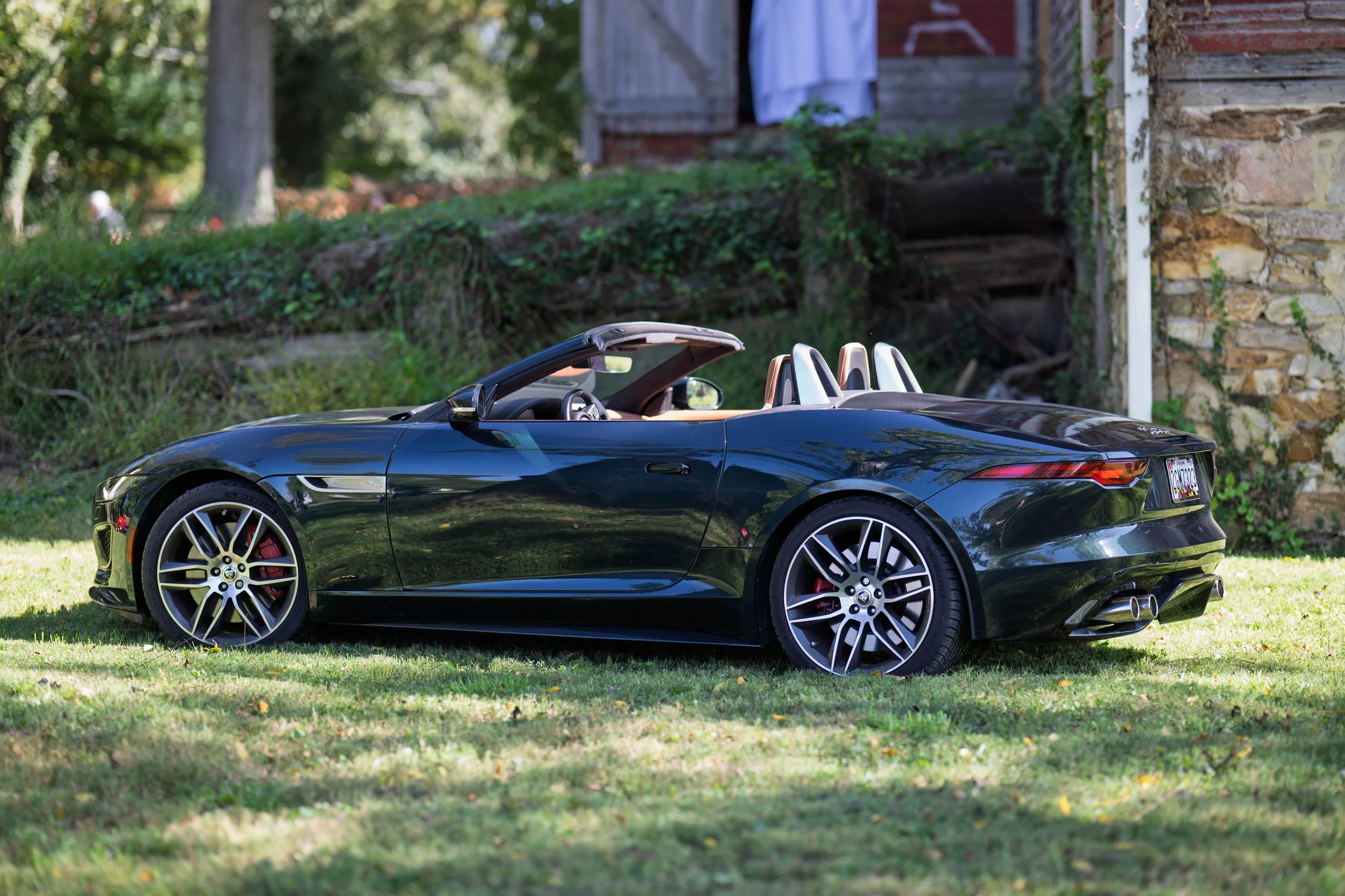 A black convertible sports car parked on a grassy area near a stone building with greenery in the background.