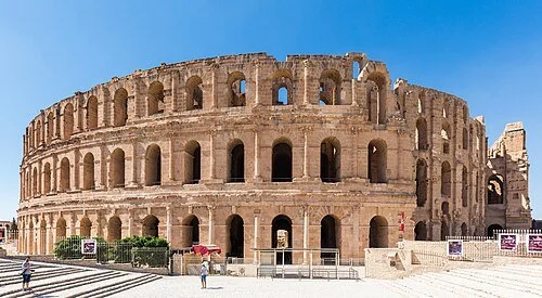 The Roman Colosseum, an ancient oval amphitheater in Rome, Italy, with tourists walking nearby on a sunny day.