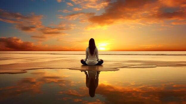 Person meditating on a beach at sunset with their reflection in the water.