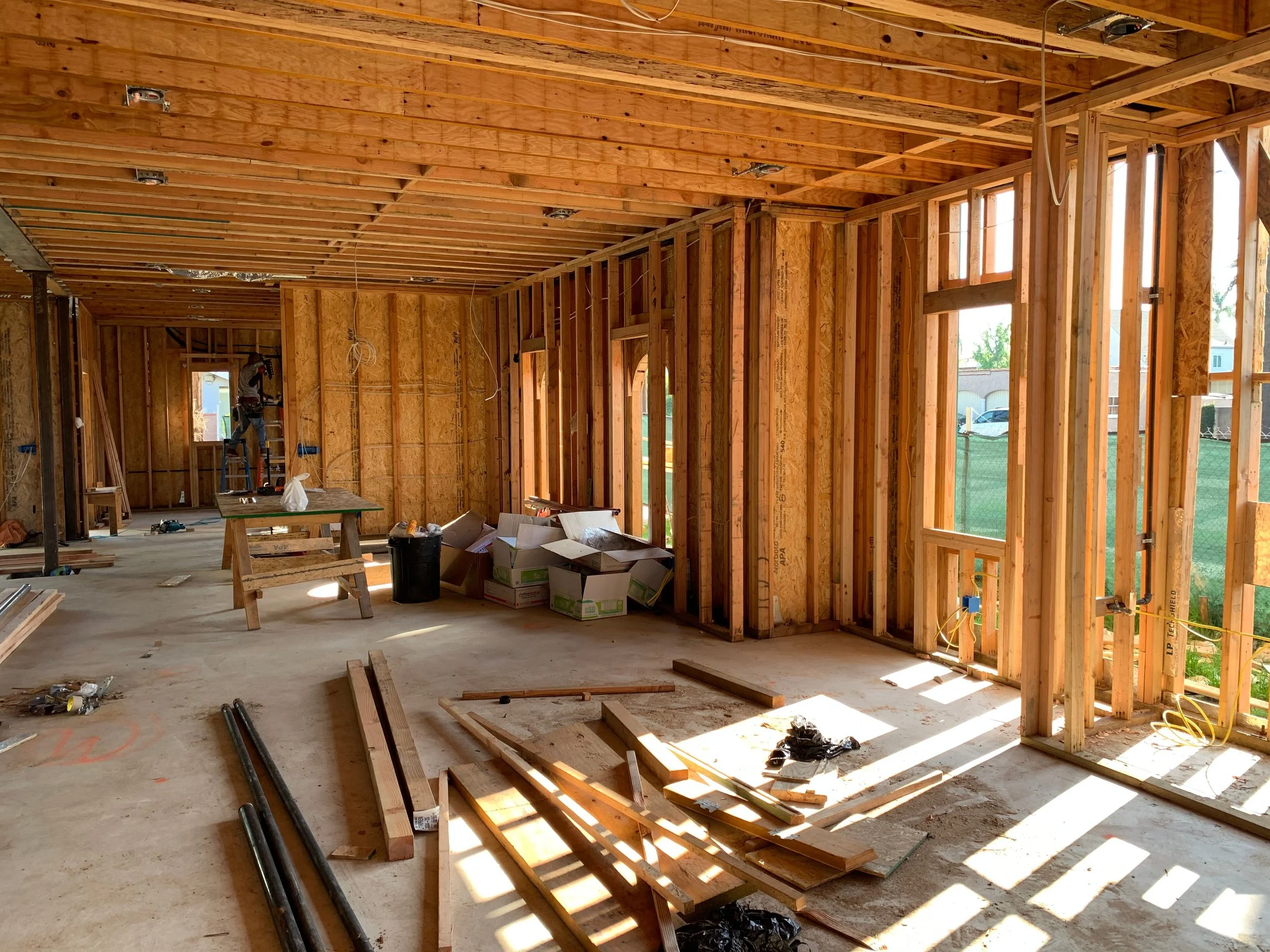 Interior of a house under construction with exposed wooden framing, construction tools, and materials scattered on the unfinished floor.
