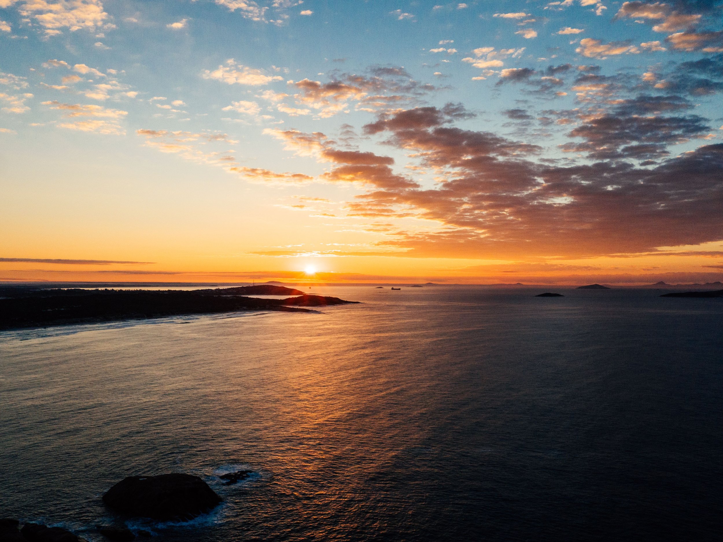 A sunset over the ocean with a partly cloudy sky and some small islands in the distance.
