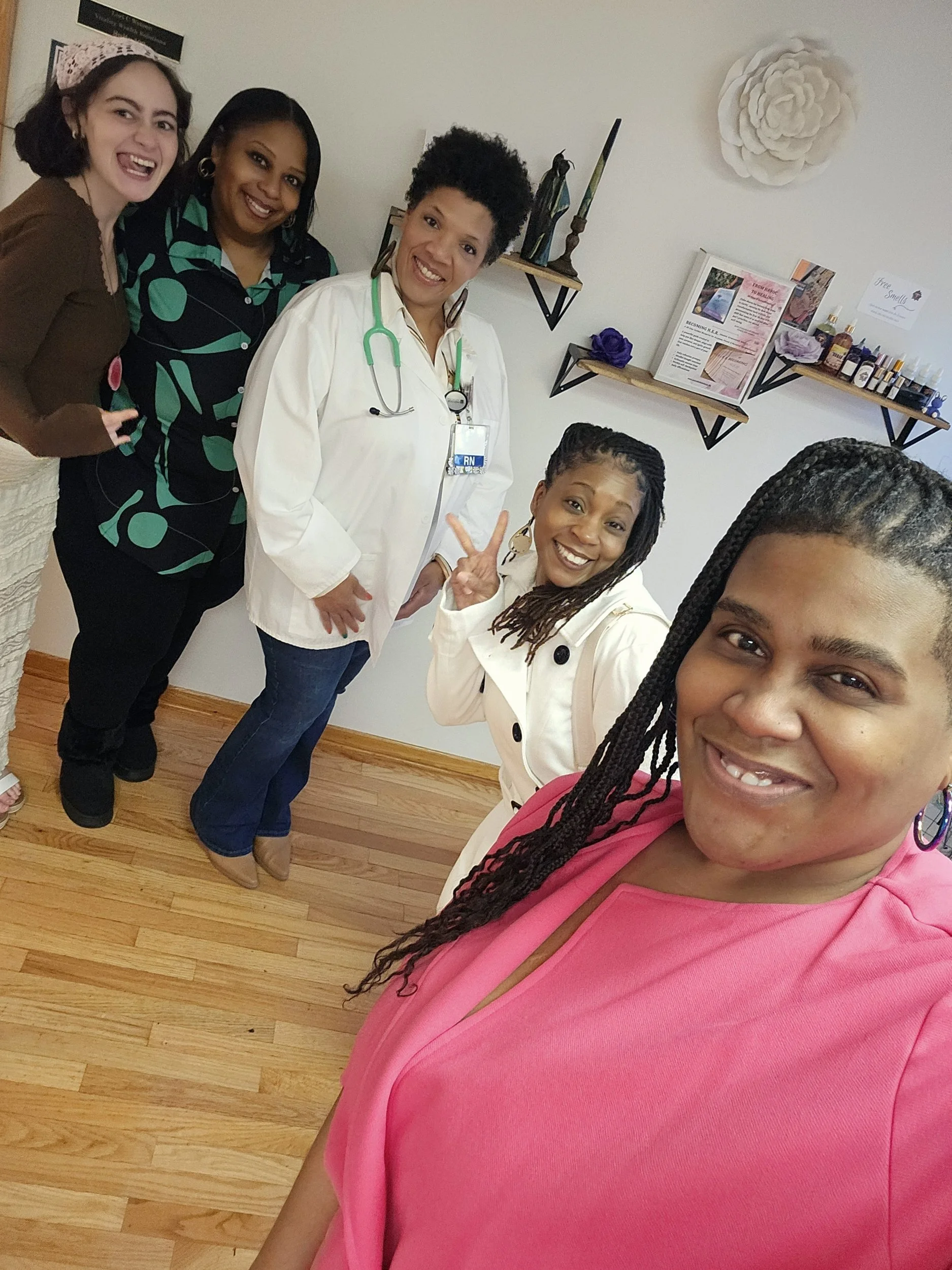 Group of five women smiling for a selfie in a room with wooden floors and shelves with various items on the walls.