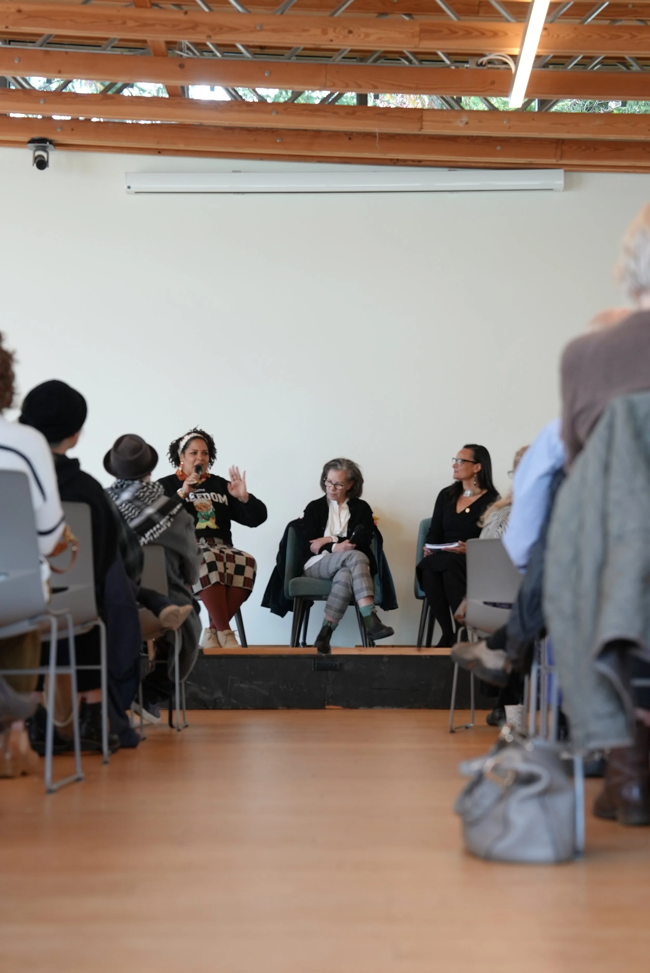 A group of people sitting and listening to an author panel discussion in a room with wooden beams, with some folding chairs visible in the foreground.