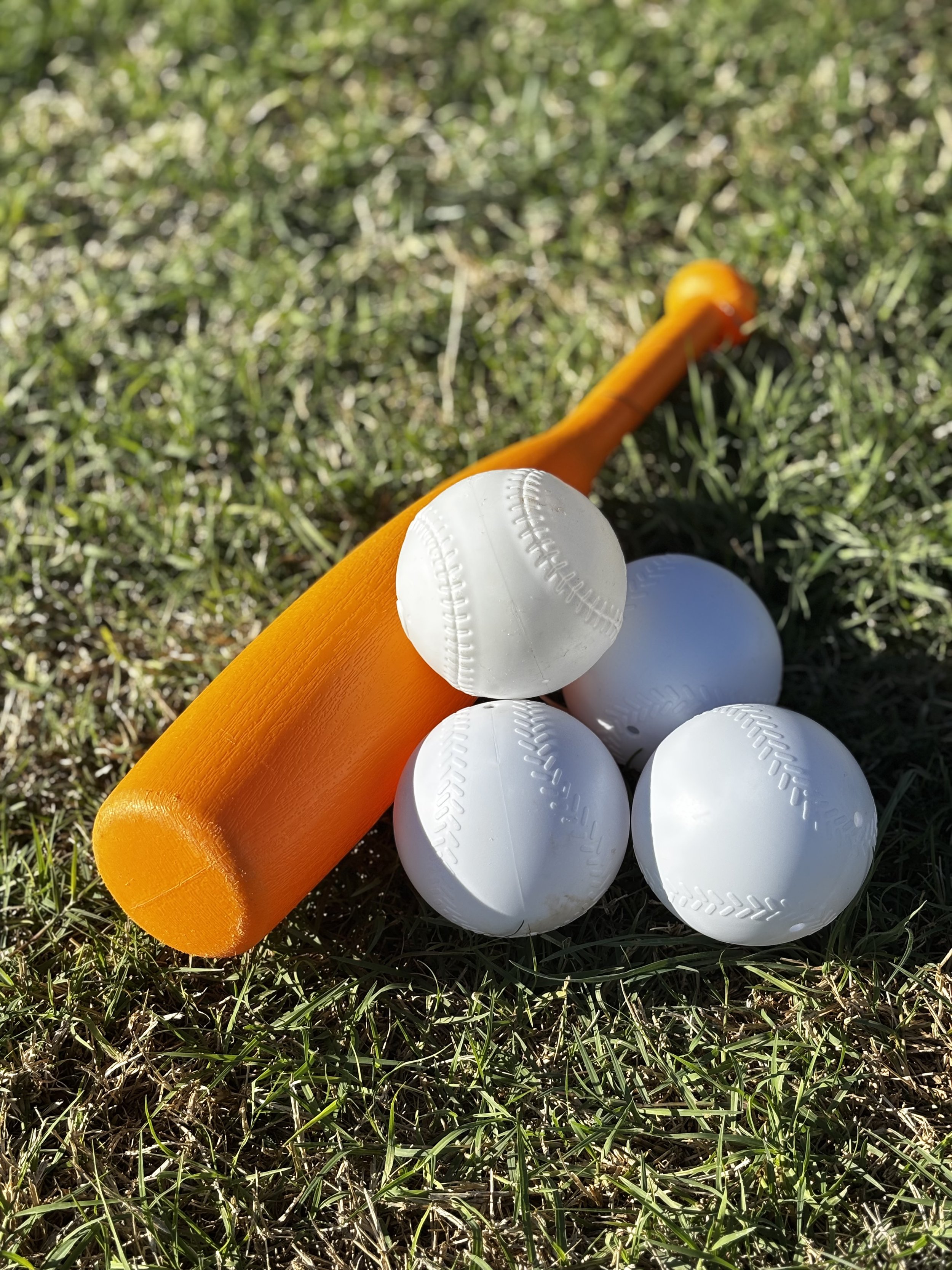A baseball bat with a bright orange handle, a white baseball, and four additional white baseballs lying on green grass.
