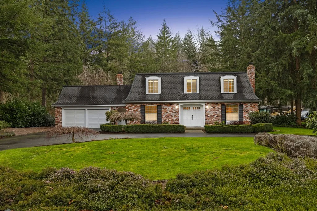 A two-story brick house with a garage, surrounded by green trees and a well-maintained lawn.