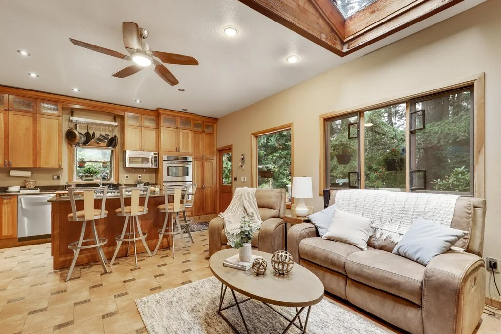 Living room and kitchen with wooden cabinets, beige furniture, large windows, and a skylight.