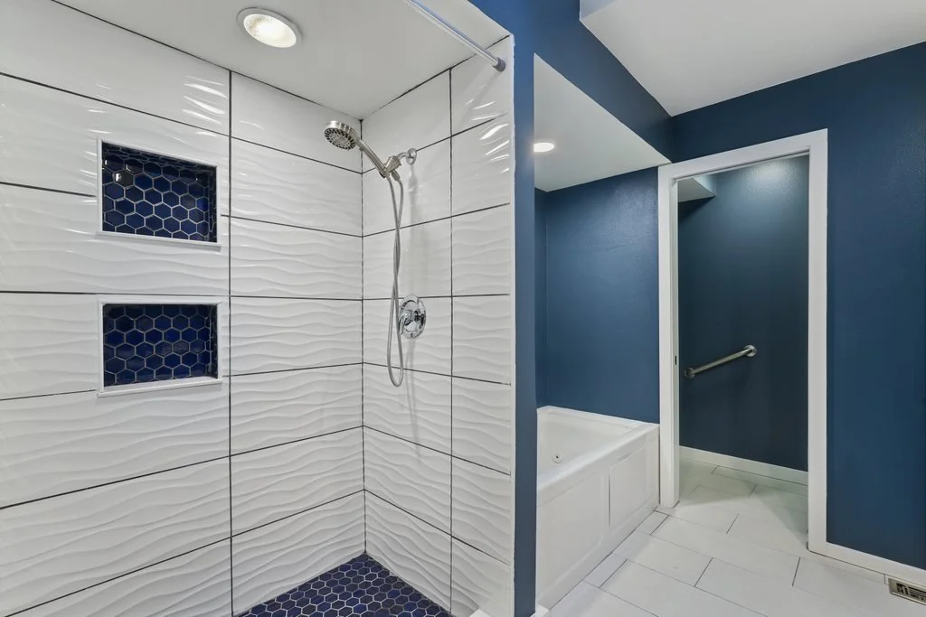 Bathroom with a walk-in shower featuring white textured tiles and two built-in niche shelves with blue hexagon tile backgrounds, and a separate bathtub next to a dark blue wall.