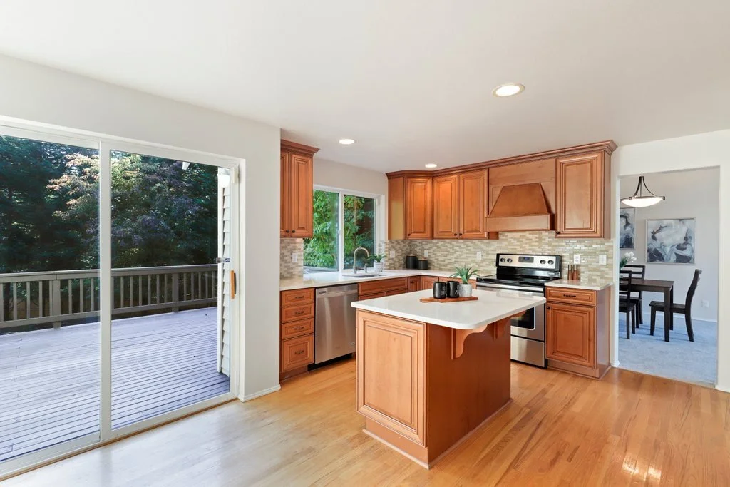 Kitchen with wooden cabinets, a central island, stainless steel appliances, and access to a deck through a sliding glass door.