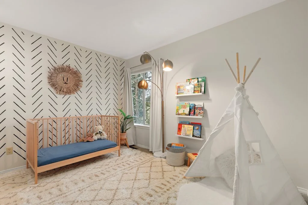 Child's bedroom with a wooden daybed, a plush teddy bear, a woven wall decor, a lamp with multiple gold and silver shades, bookshelves, a window with curtains, and a white teepee