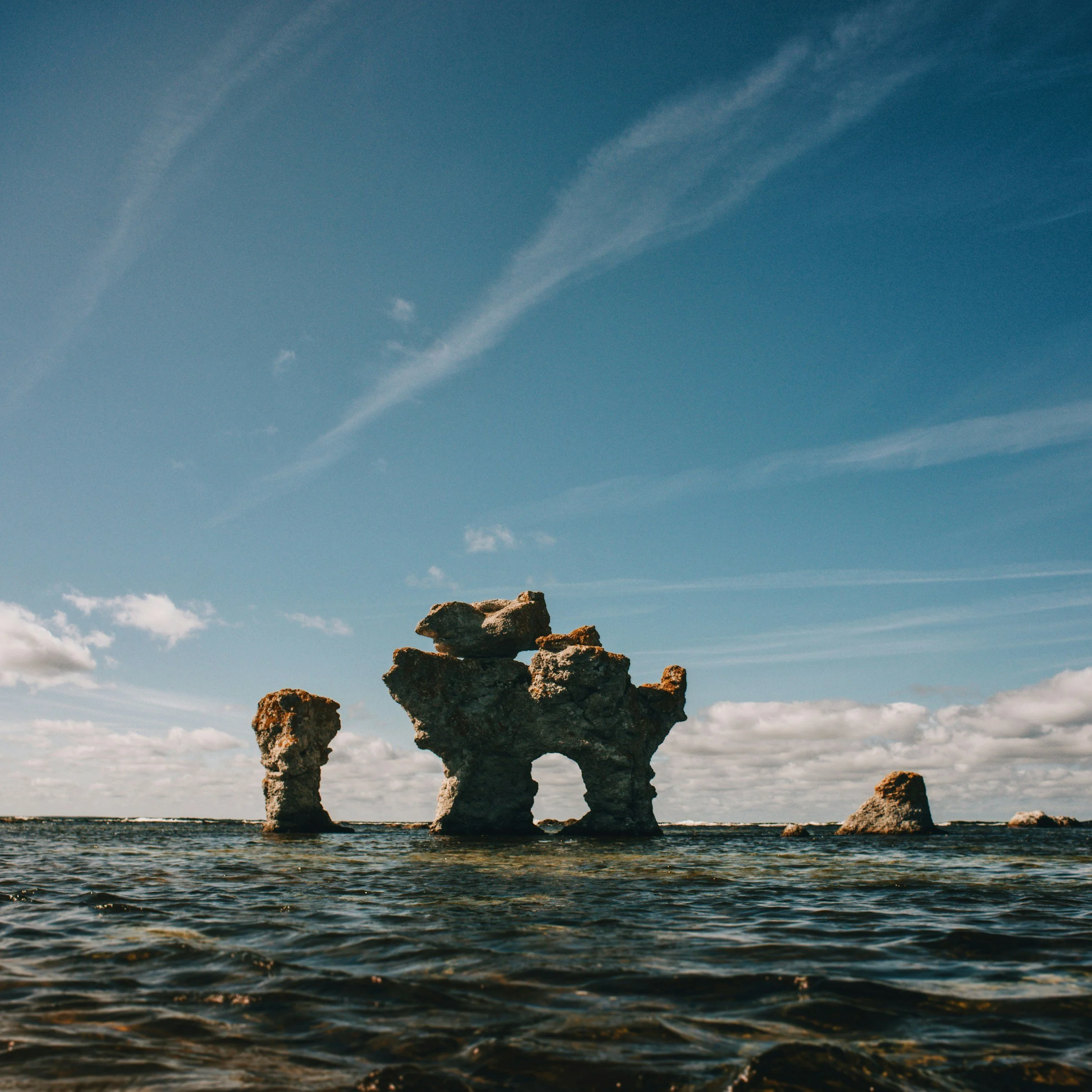 Foto av en solbelyst rauk ute i havet, under en huvudsakligen blå himmel.