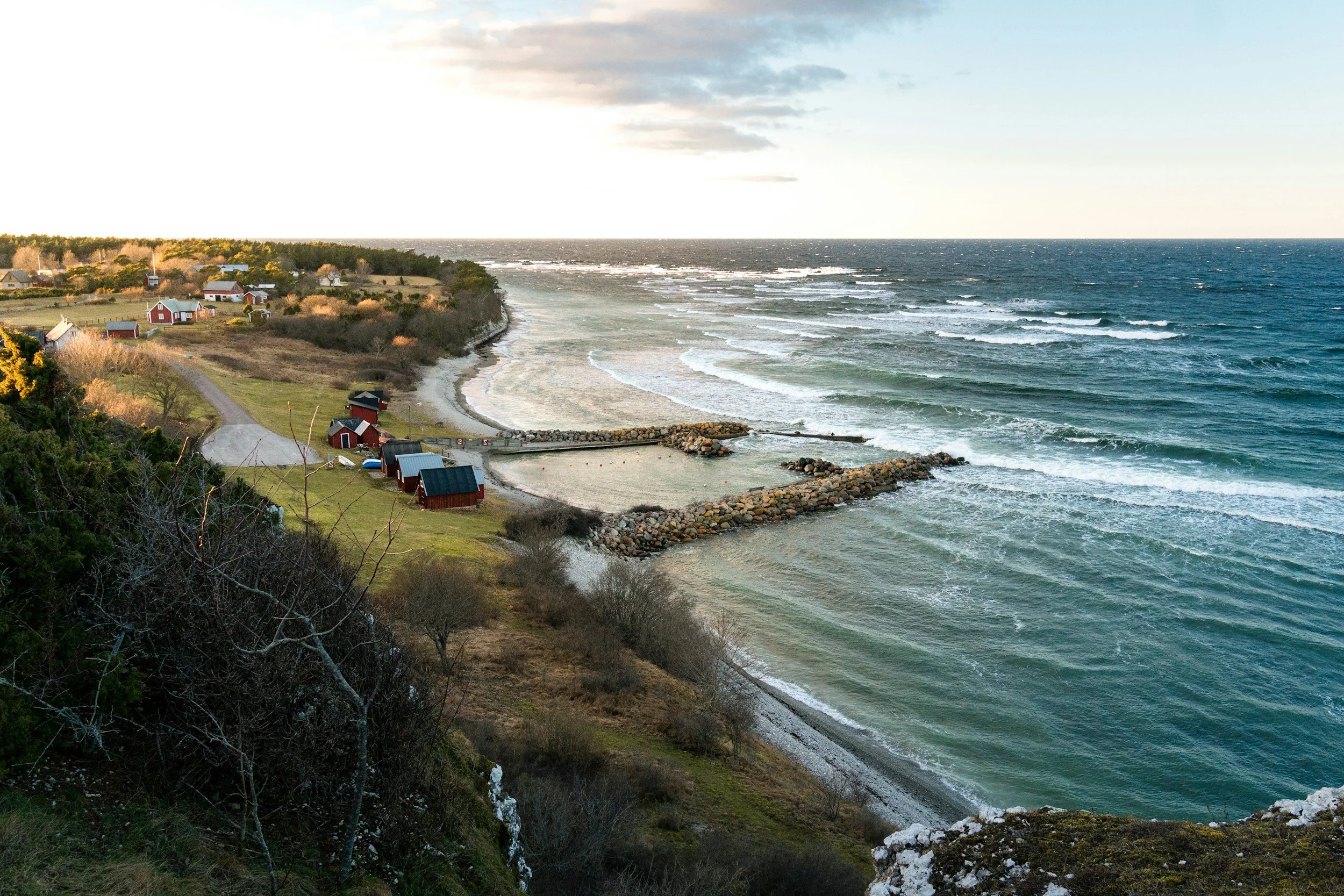 En kustlinje med små röda hus och en klippa med vågor som slår mot stranden, under en molnig himmel.