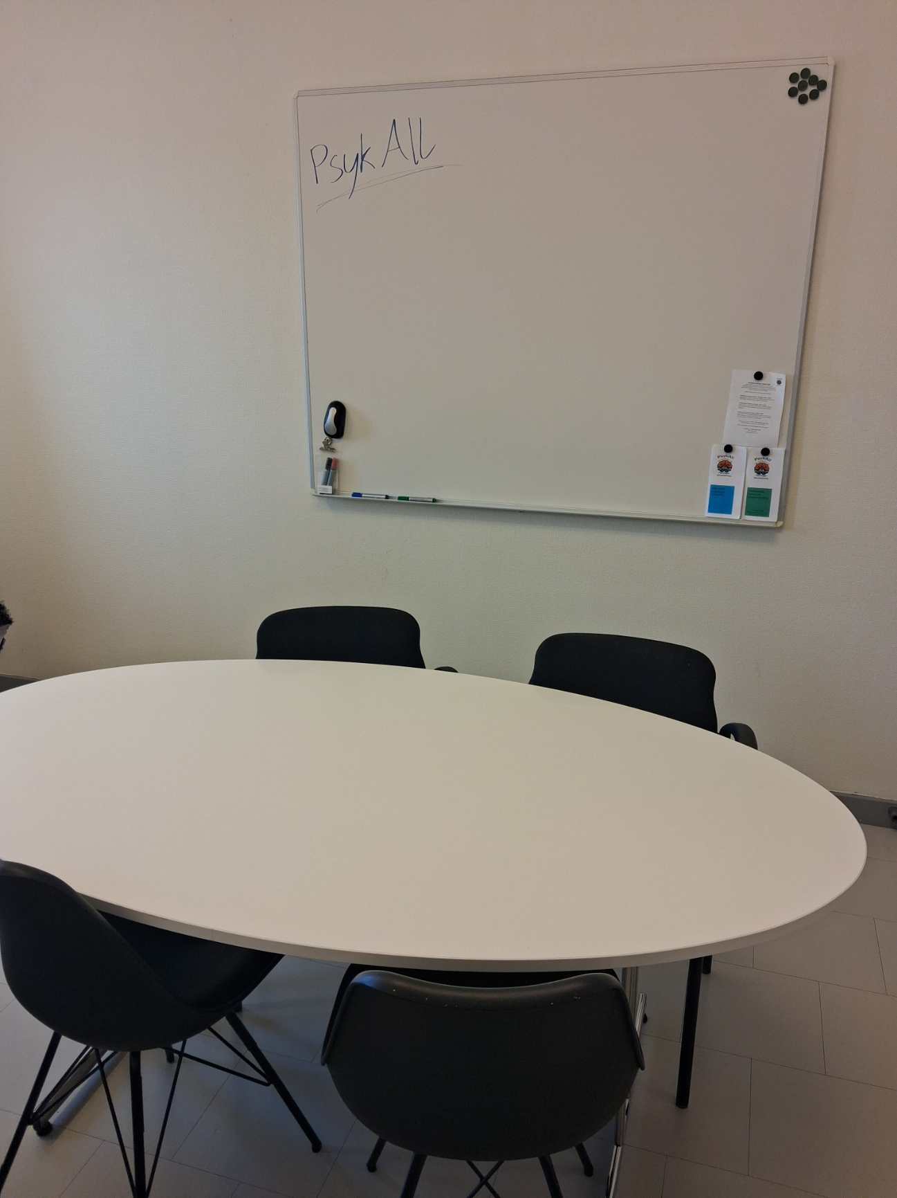 Ett ovalt bord med fyra stolar runt, och i bakgrunden en whiteboard där det står PsykAll skrivet med blå och grön penna