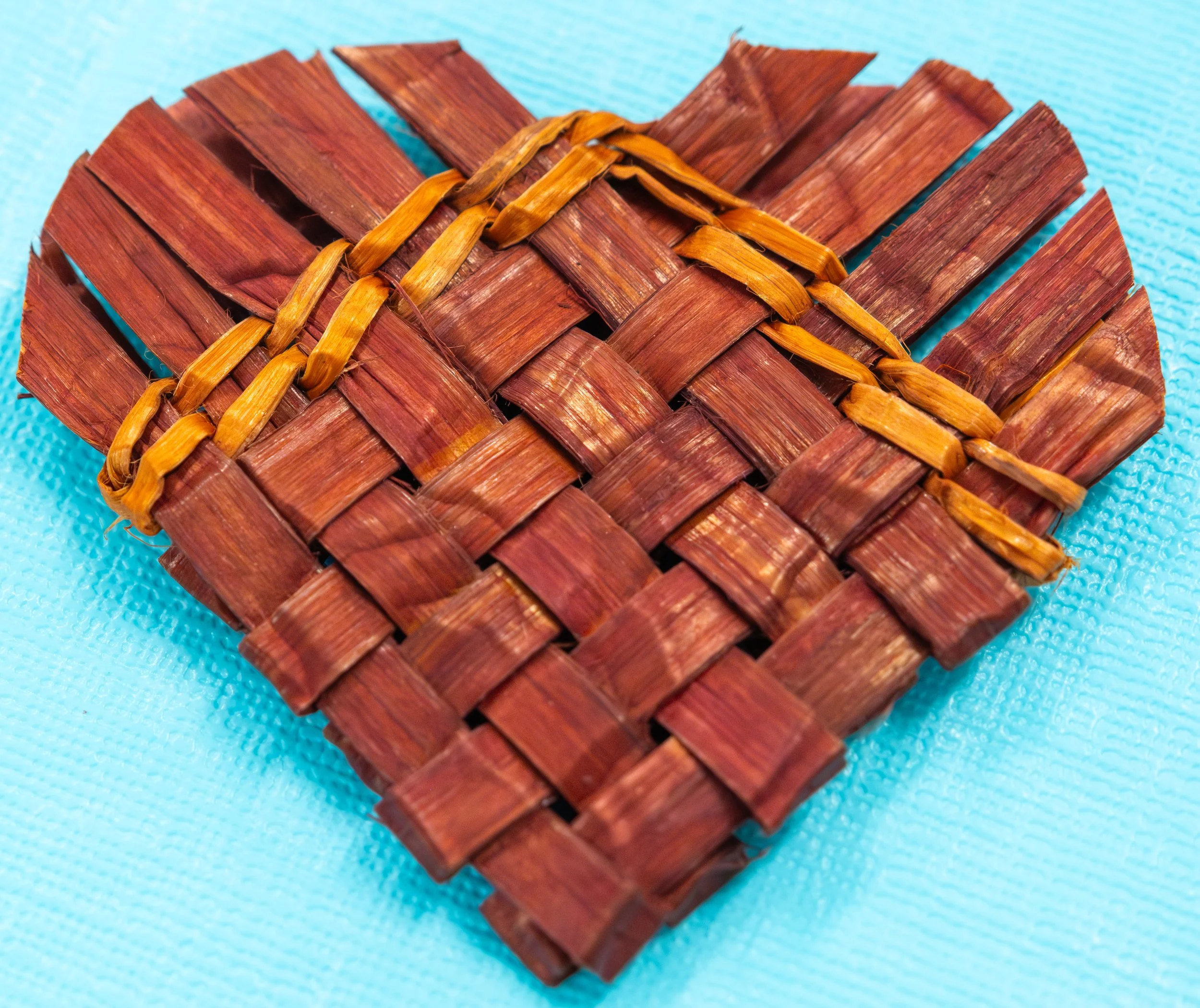 A heart-shaped woven red cedar ornament on a light blue background.