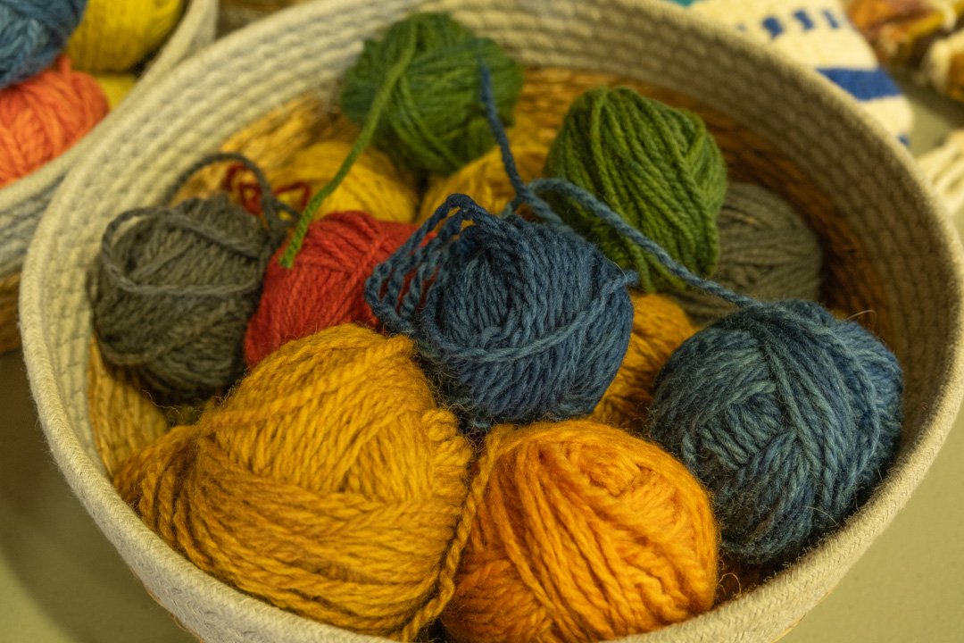 A basket filled with various coloured balls of yarn, including yellow, orange, gray, green, red, and blue.