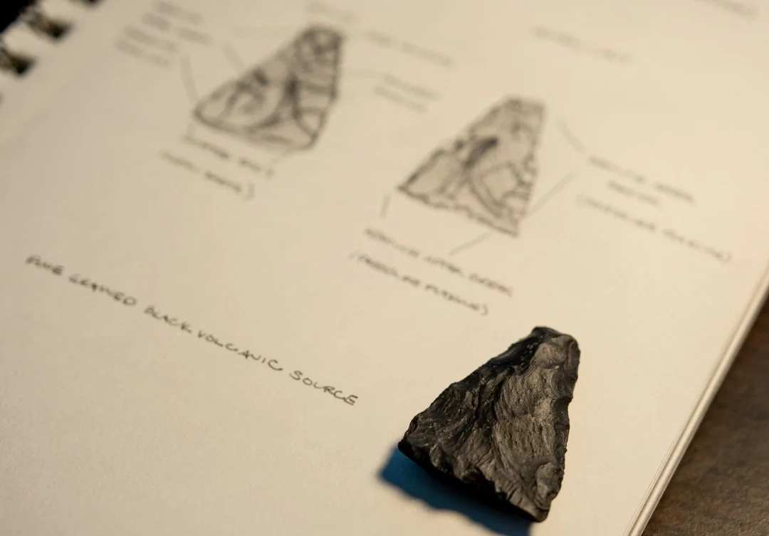 A black volcanic rock biface on an open book showing diagrams and text about the biface.
