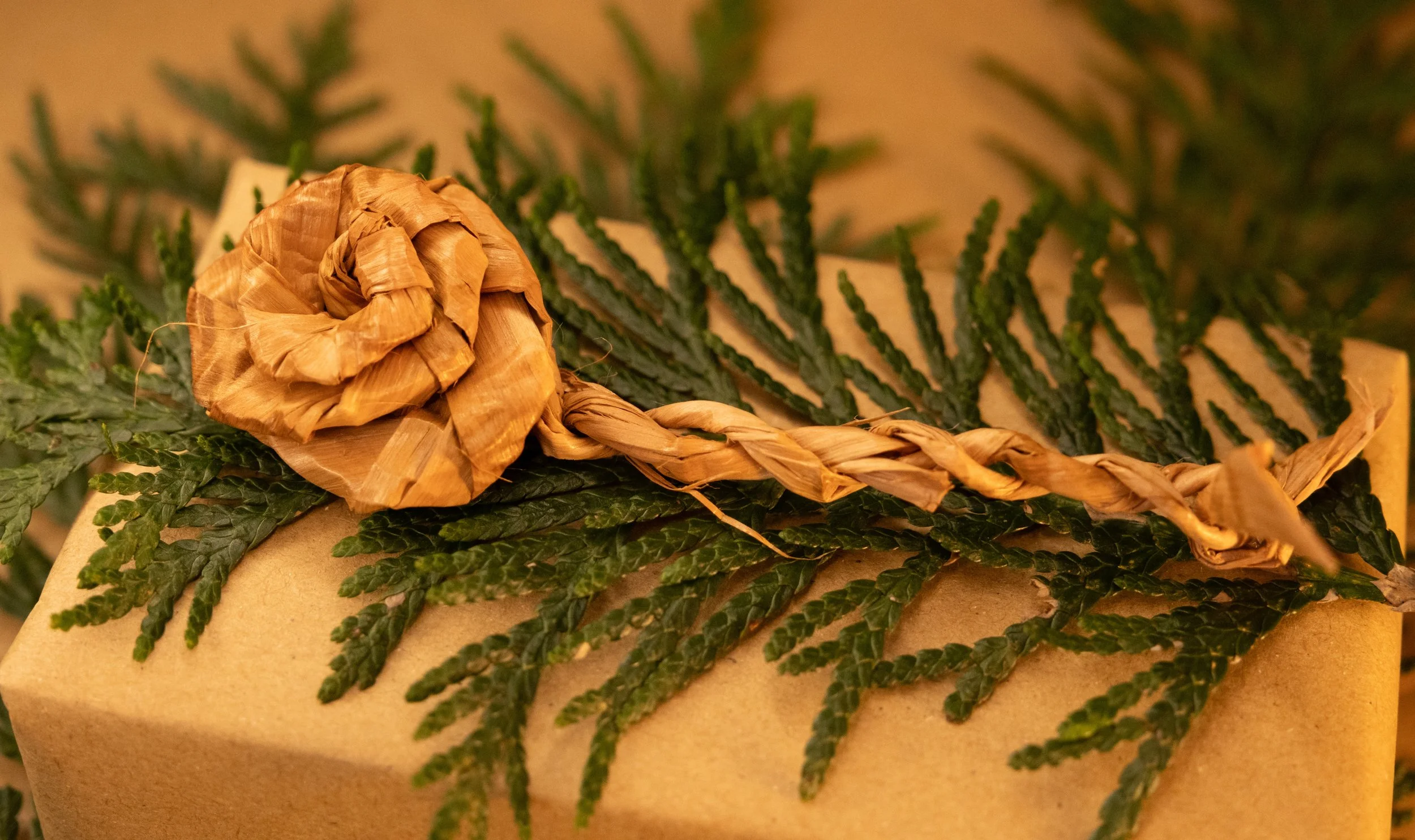 Close-up of a box with a brown paper cover, decorated with a sprig of cedar and a rose made of twisted red cedar fibers.