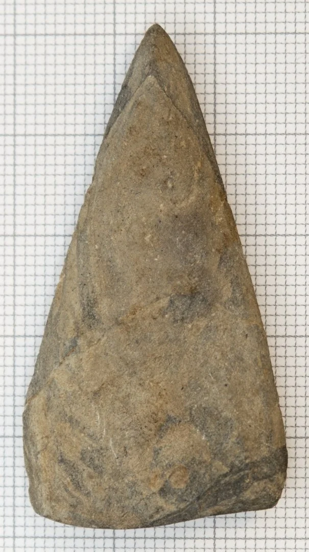 A large, pointed stone tool or projectile point placed on a gridded background for scale.