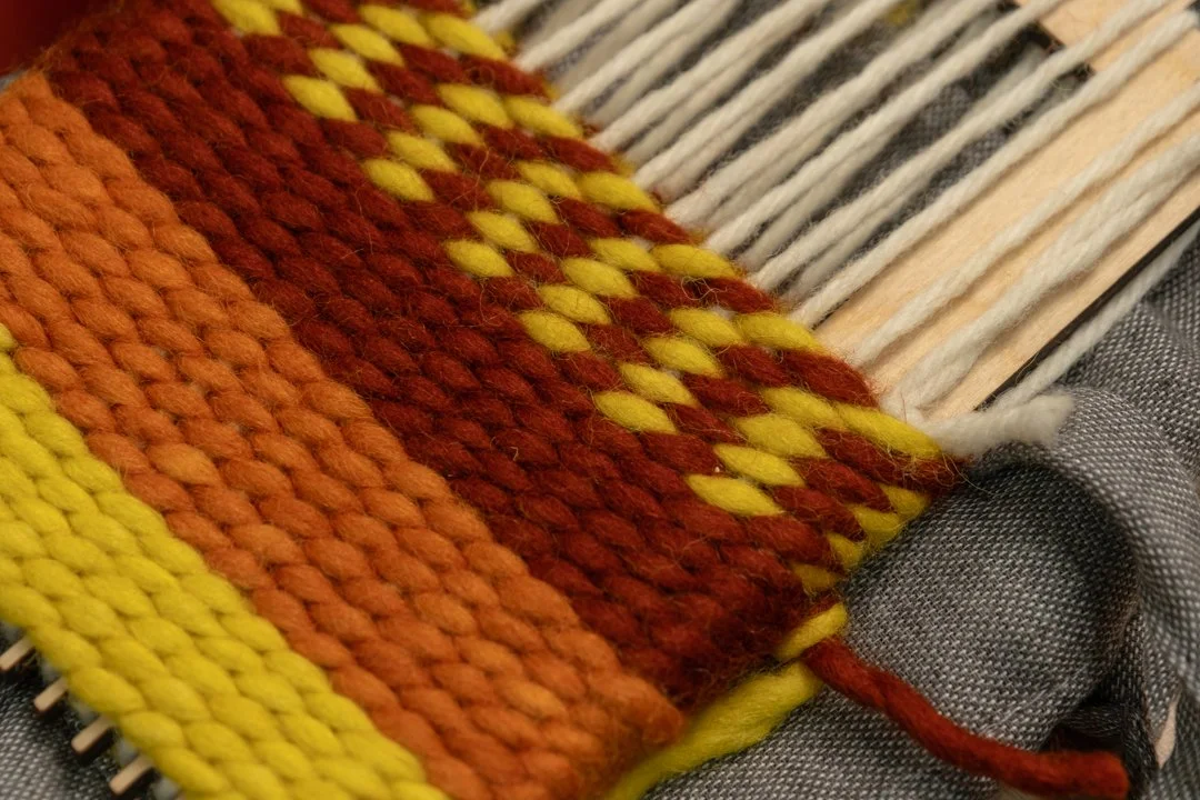 Close-up of a weaving loom with colorful yarns in red, yellow, orange, and beige.