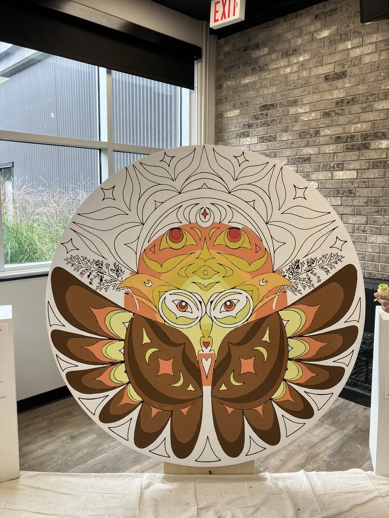 Circular canvas of artwork featuring geometric and symmetrical patterns in warm colours of brown, orange, yellow, and cream, displayed indoors near a window and brick wall.