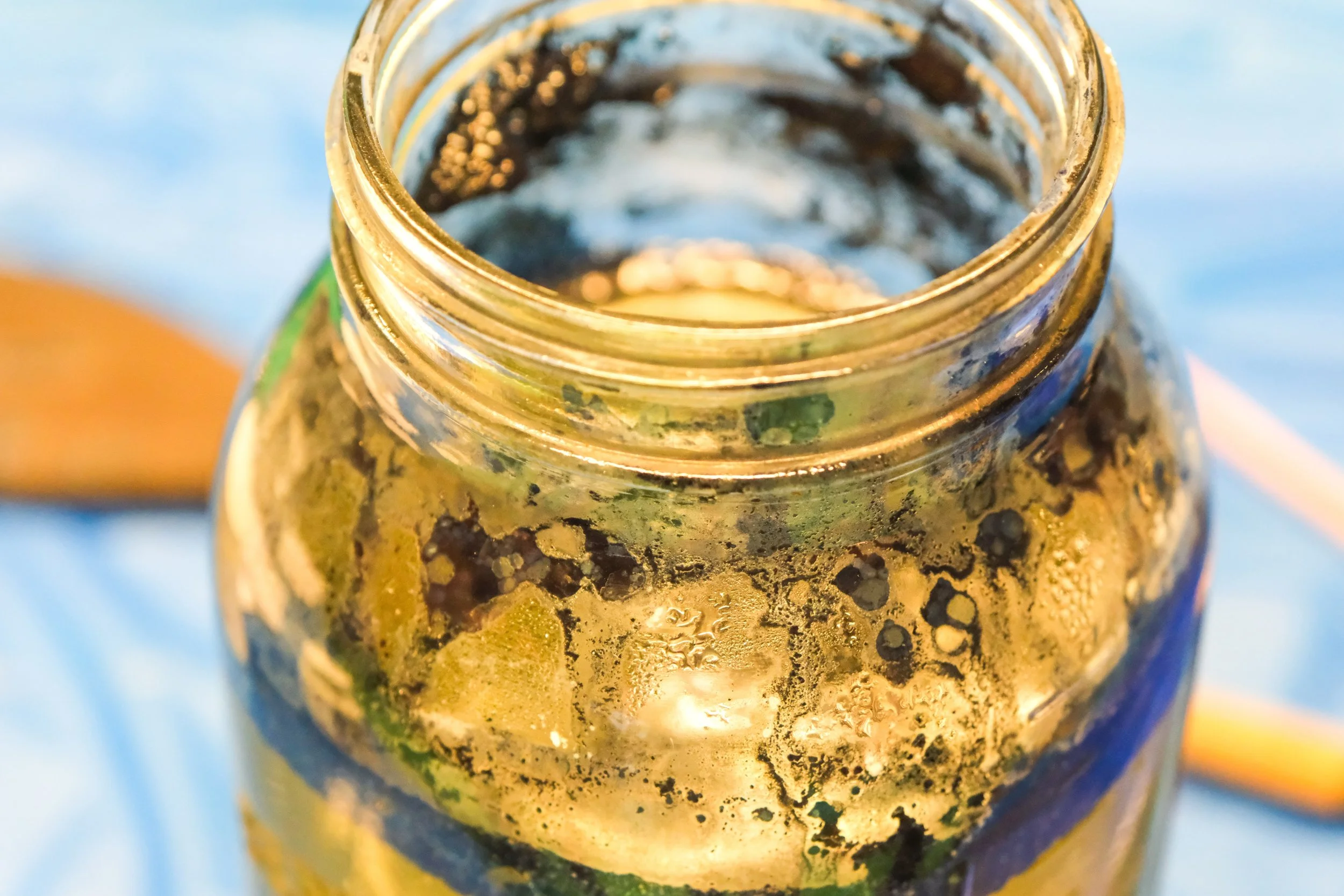 Close-up of an open glass jar with indigo dye, set on a blue surface.