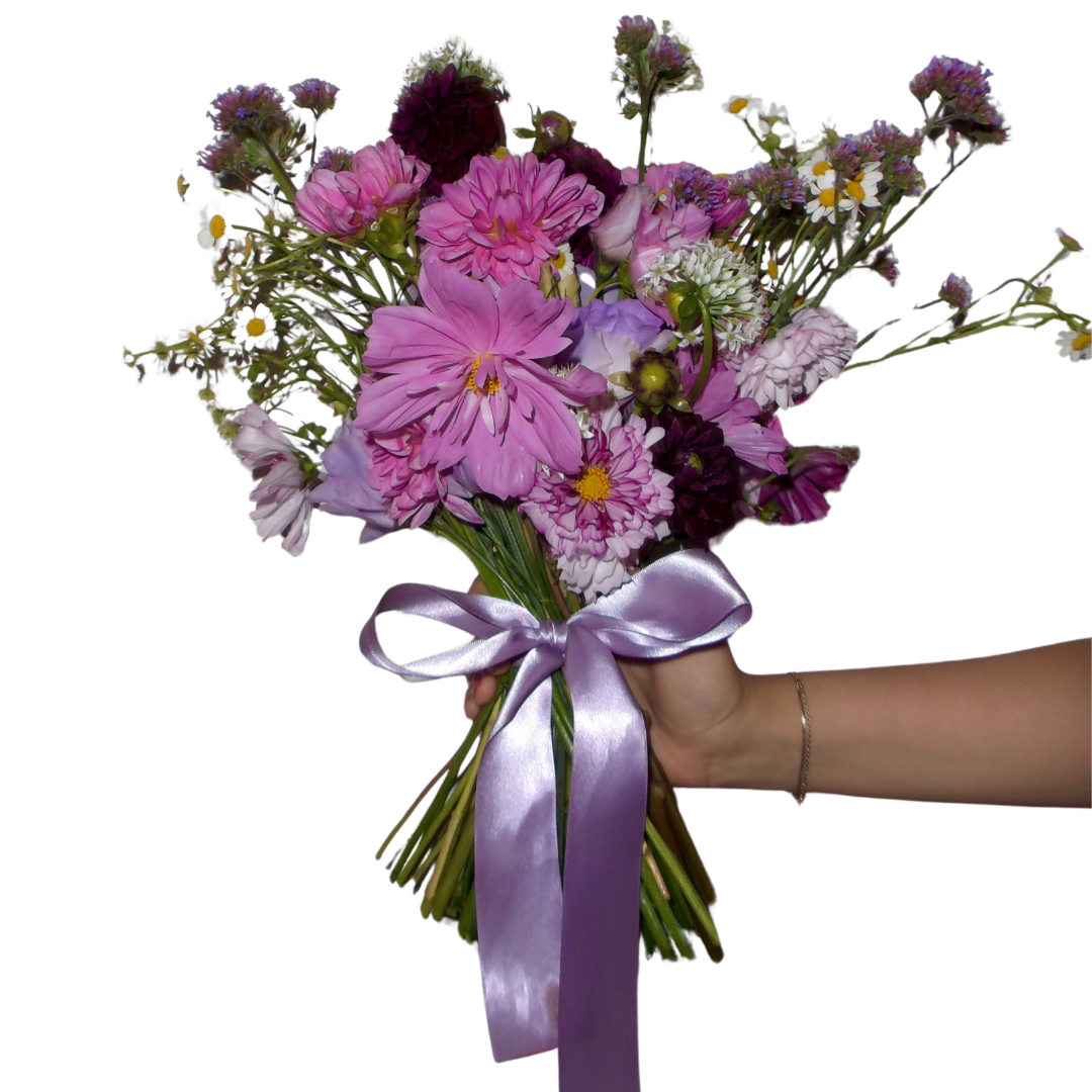 Hand holding a bouquet of pink, purple, white, and dark-colored flowers tied with a lavender satin ribbon.