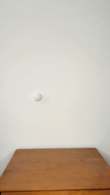 A ping pong ball bouncing in front of a white wall above a wooden table.