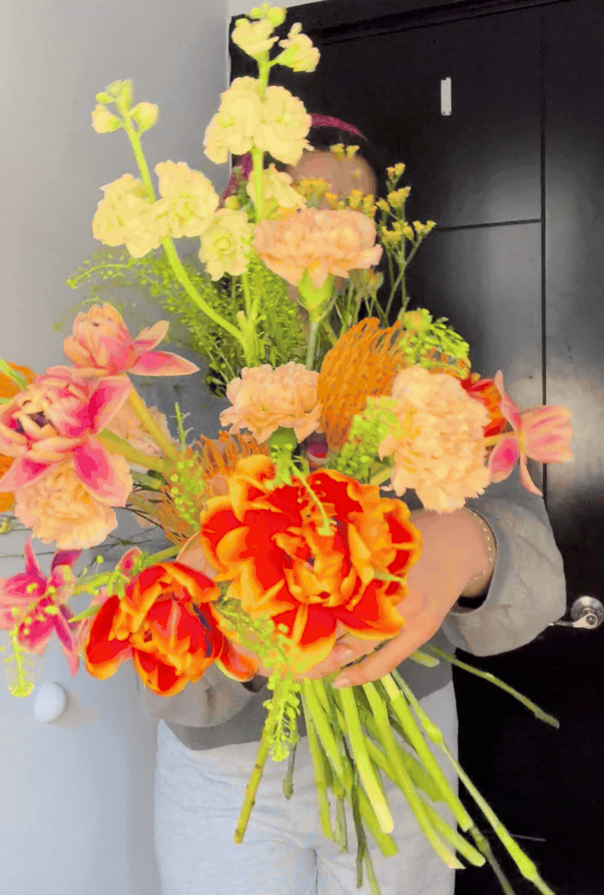 Person holding a colorful bouquet of flowers with orange, pink, and cream-colored blooms.