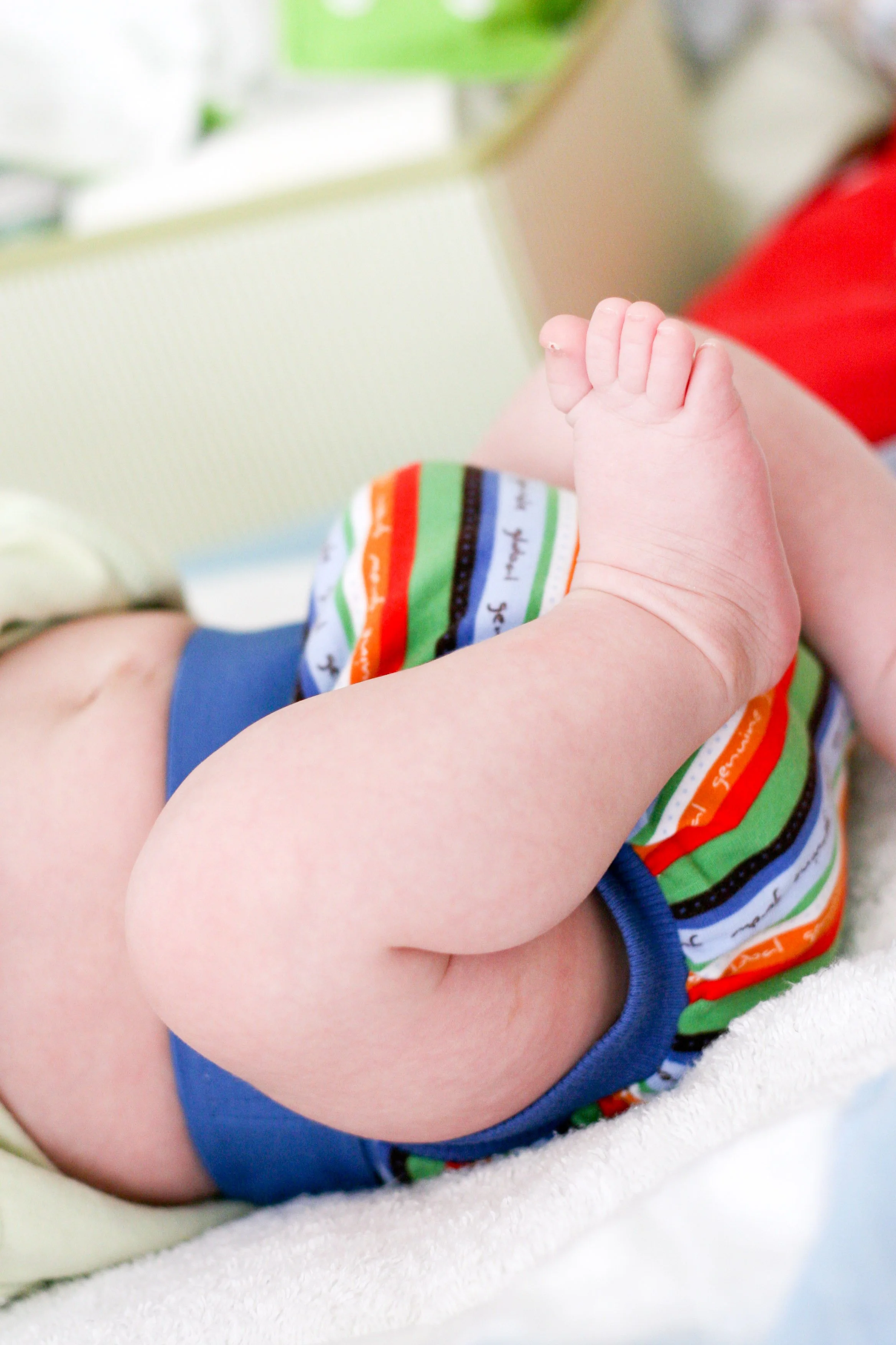 Close-up of an infant lying on a soft surface, wearing colorful striped underwear, with a focus on the tiny foot.