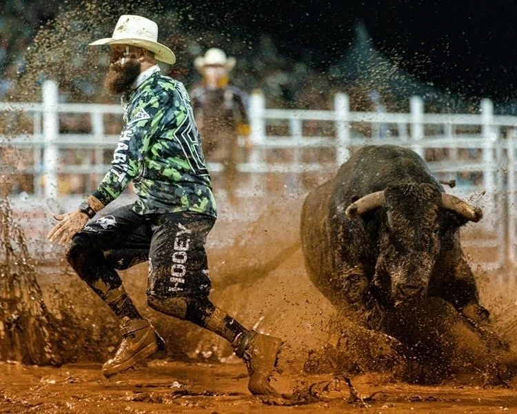 Weston Rutkowski freestyle bullfighter evading bull in muddy arena at professional BFO competition — Bearded Elf Co. founder Granbury Texas