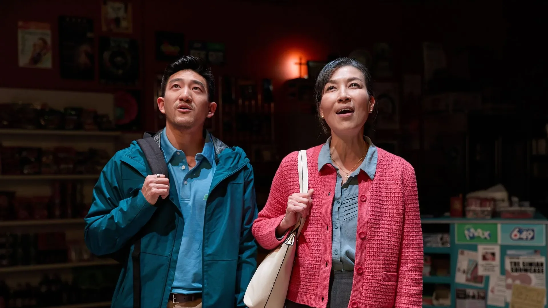 A man and woman looking up in a store, with shelves and posters in the background.