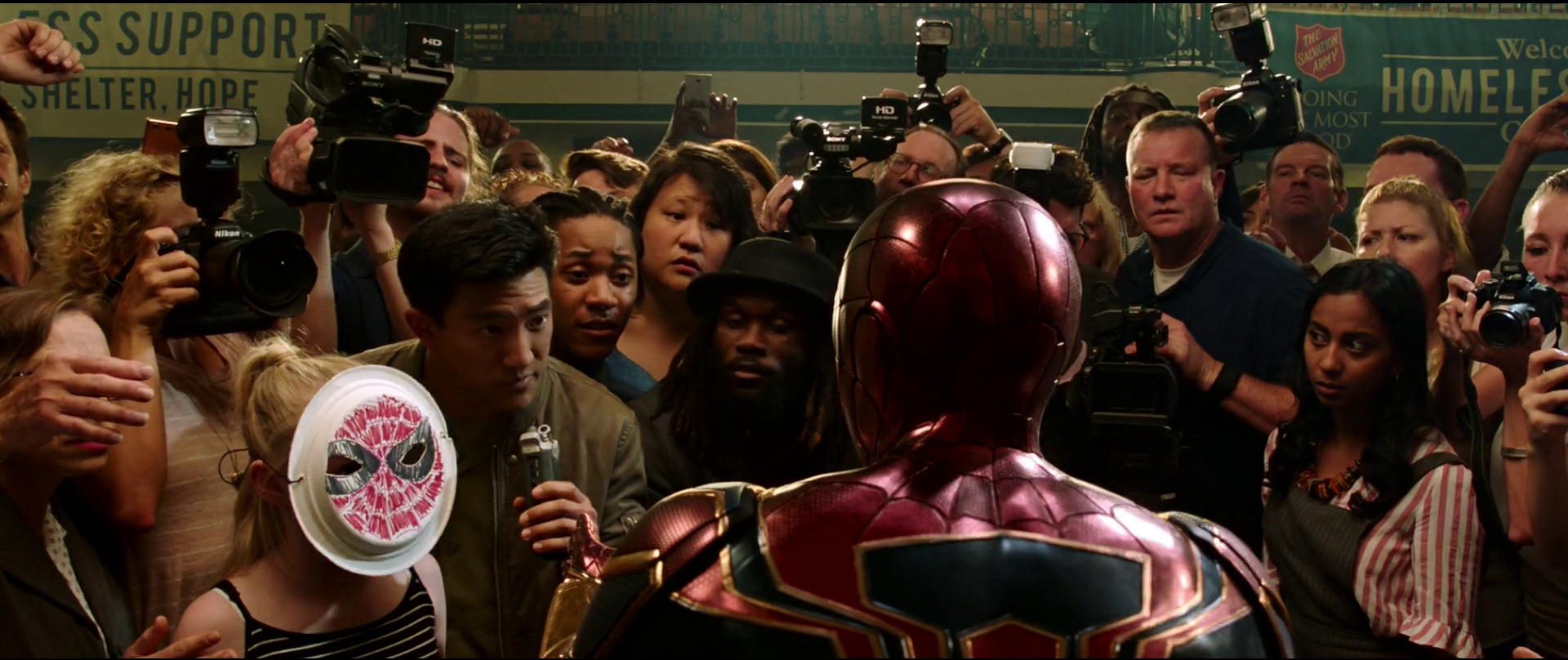 Spider-Man in his superhero costume appears to be addressing a crowd of reporters and onlookers at a public event or press conference.
