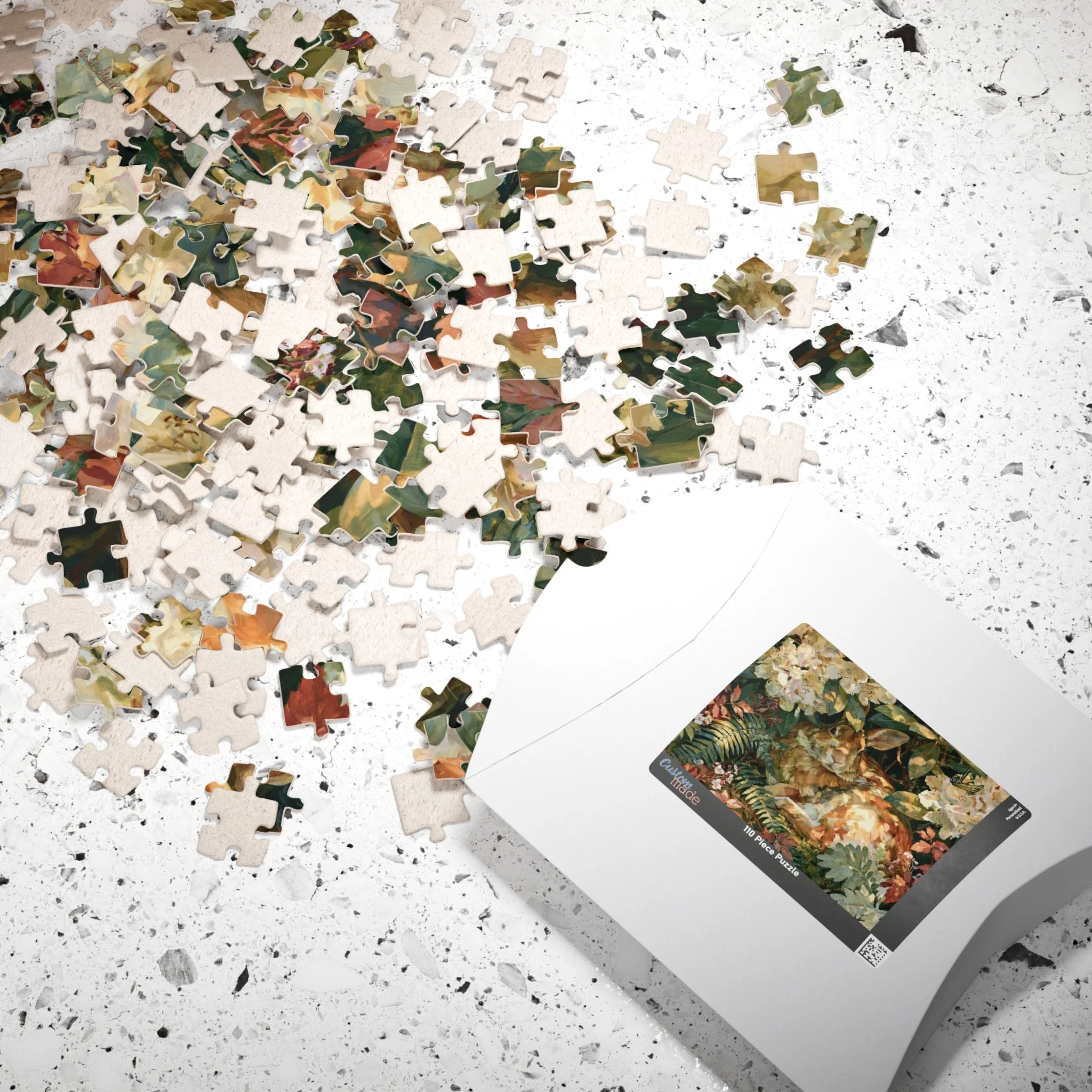 Rabbit in the Rhododendron jigsaw puzzle pieces and box with original Lakehouse artwork of an Eastern cottontail hidden in rhododendron, ferns, moss, and warm woodland light