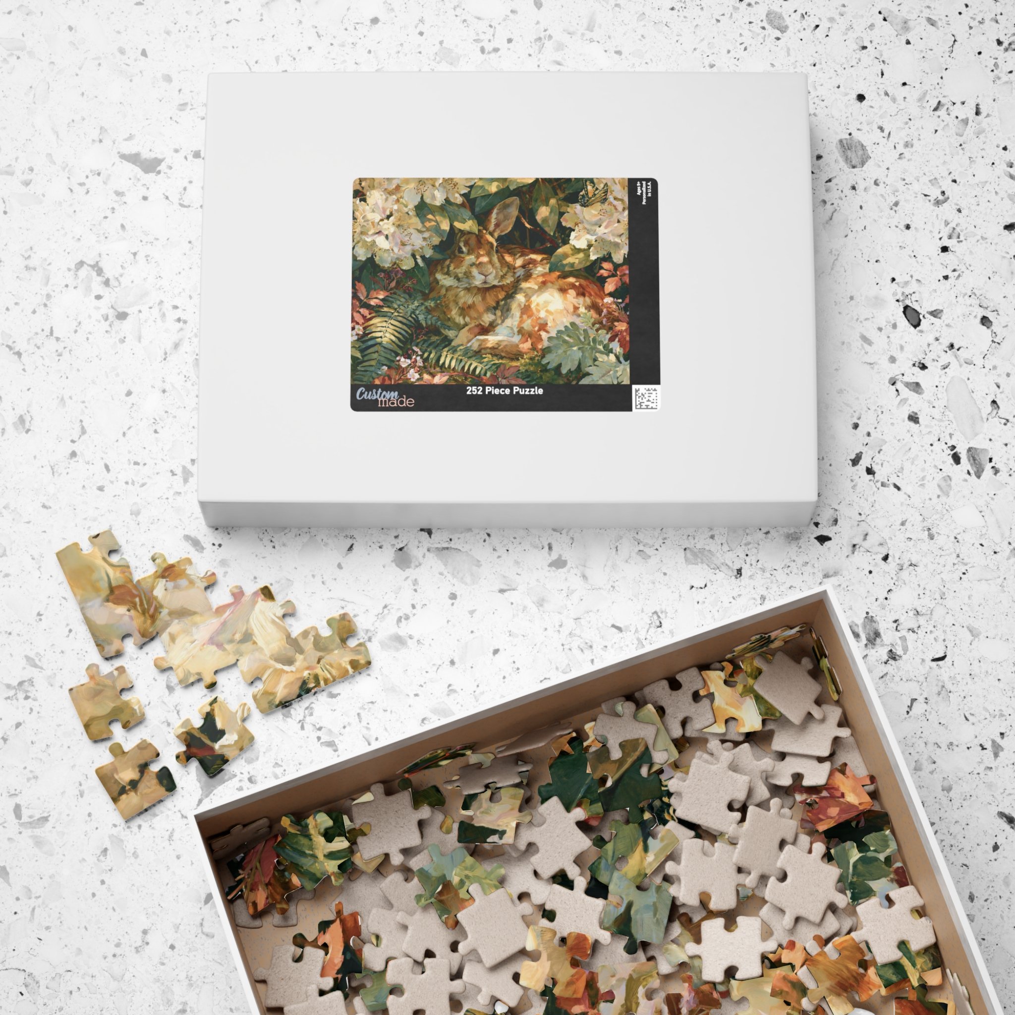 Rabbit in the Rhododendron jigsaw puzzle pieces and box with original Lakehouse artwork of an Eastern cottontail hidden in rhododendron, ferns, moss, and warm woodland light