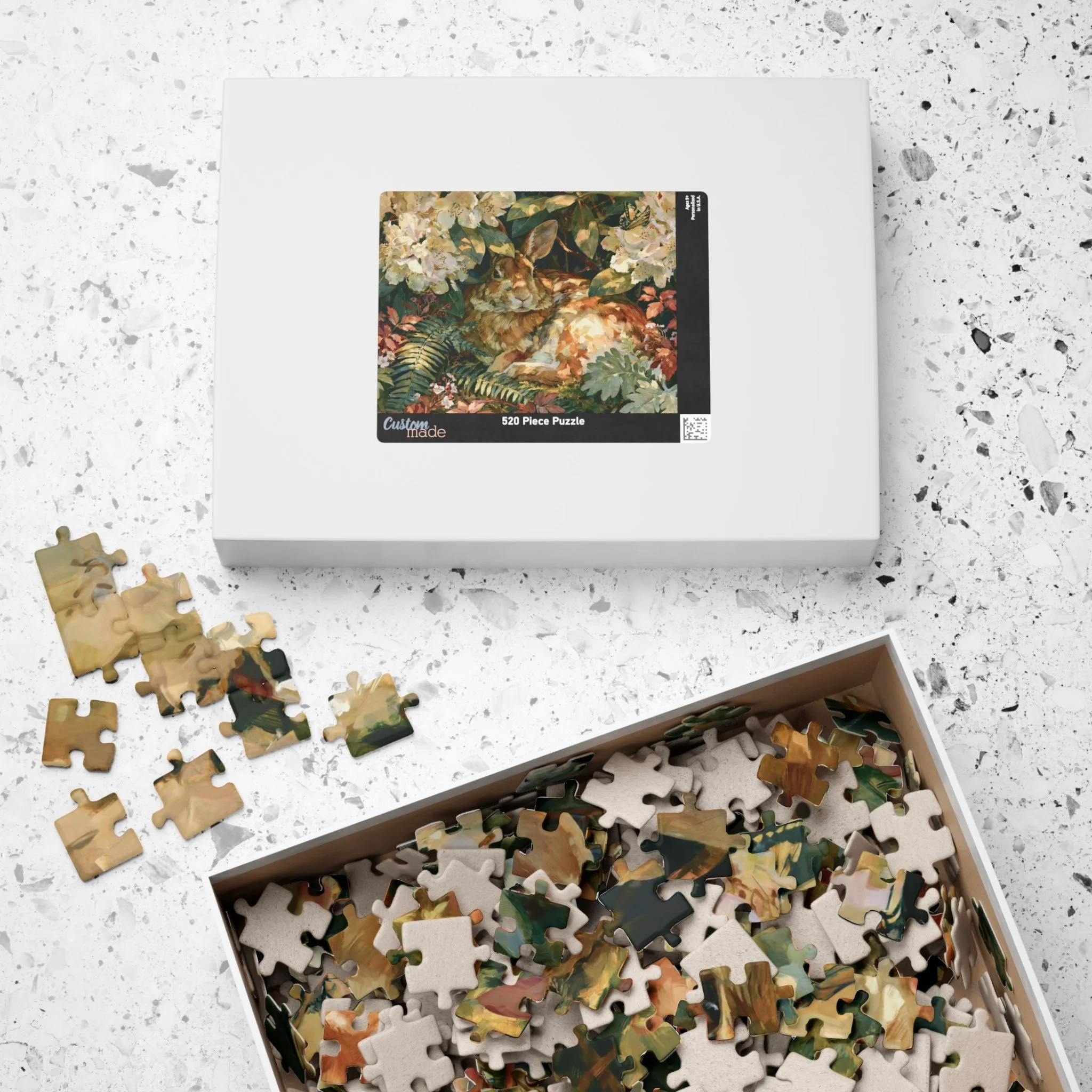 Rabbit in the Rhododendron jigsaw puzzle pieces and box with original Lakehouse artwork of an Eastern cottontail hidden in rhododendron, ferns, moss, and warm woodland light