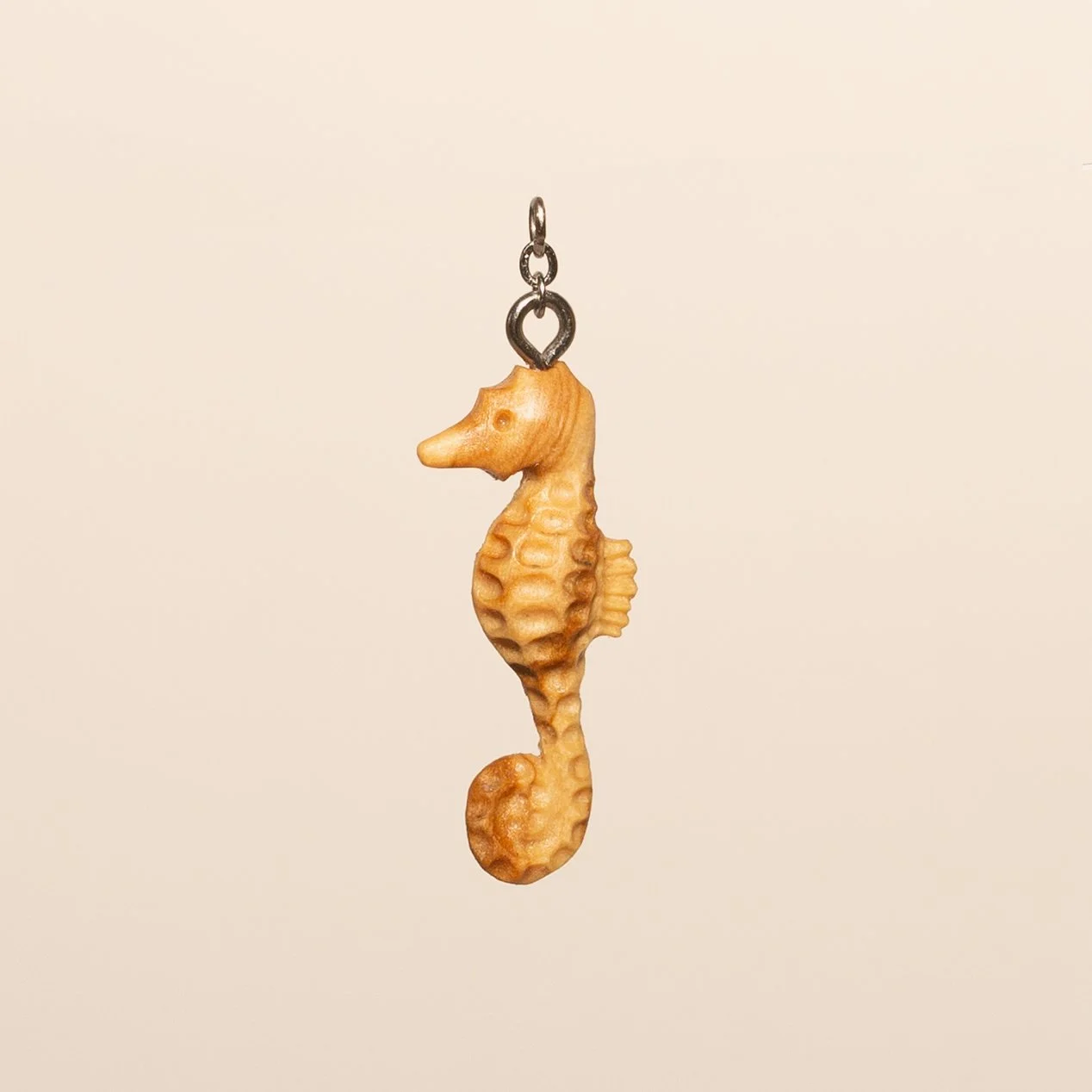 A pendant shaped like a seahorse with a textured surface, hanging from a small metal loop.
