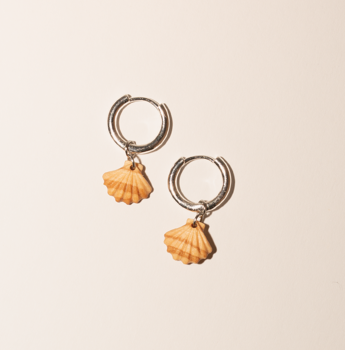 Silver hoop earrings with small shell charms on a plain background.