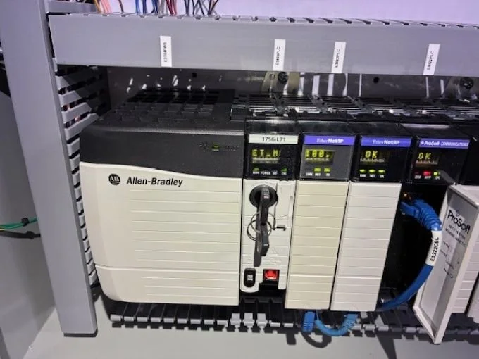 Close-up of industrial automation equipment, including Allen-Bradley controller and network modules, installed on a metal rack in a control panel.