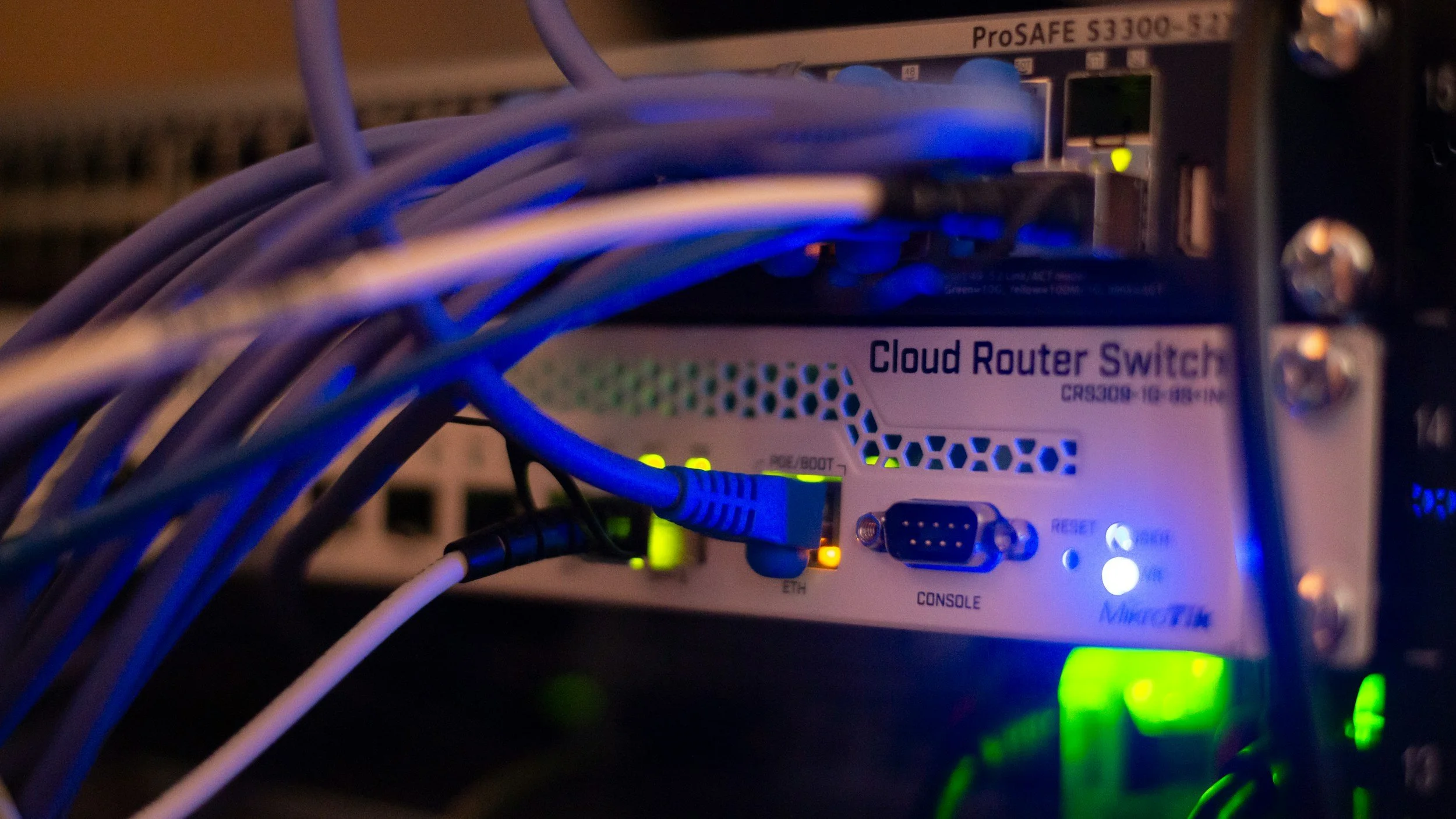 Close-up of a network equipment rack with a cloud router switch labeled 'Cloud Router Switch' connected to multiple Ethernet cables with illuminated indicator lights.