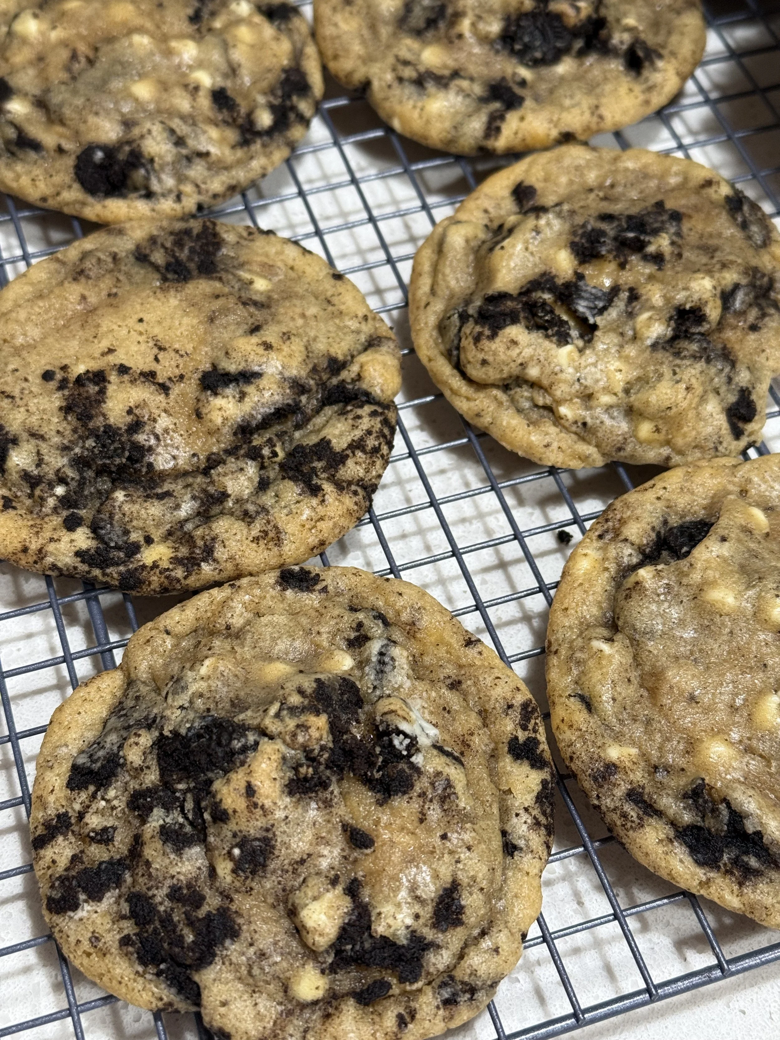 Four freshly baked chocolate chip cookies on a cooling rack.