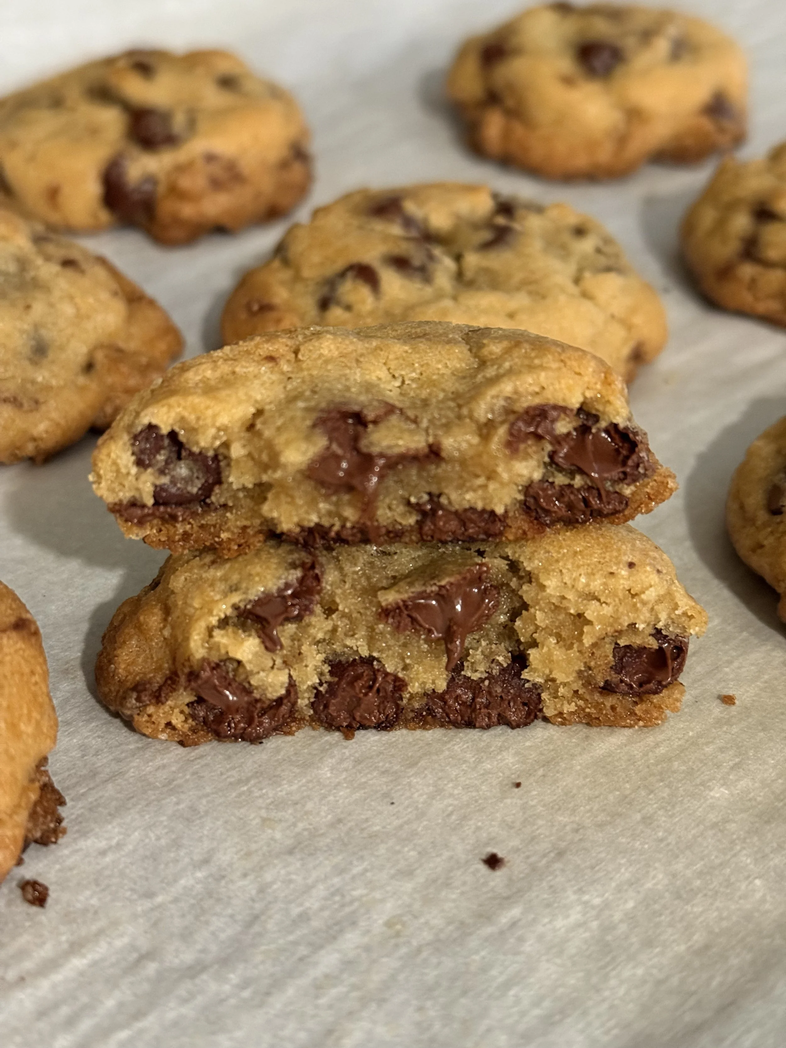 Close-up of chocolate chip cookies, with one cookie broken in half showing melted chocolate inside, on parchment paper