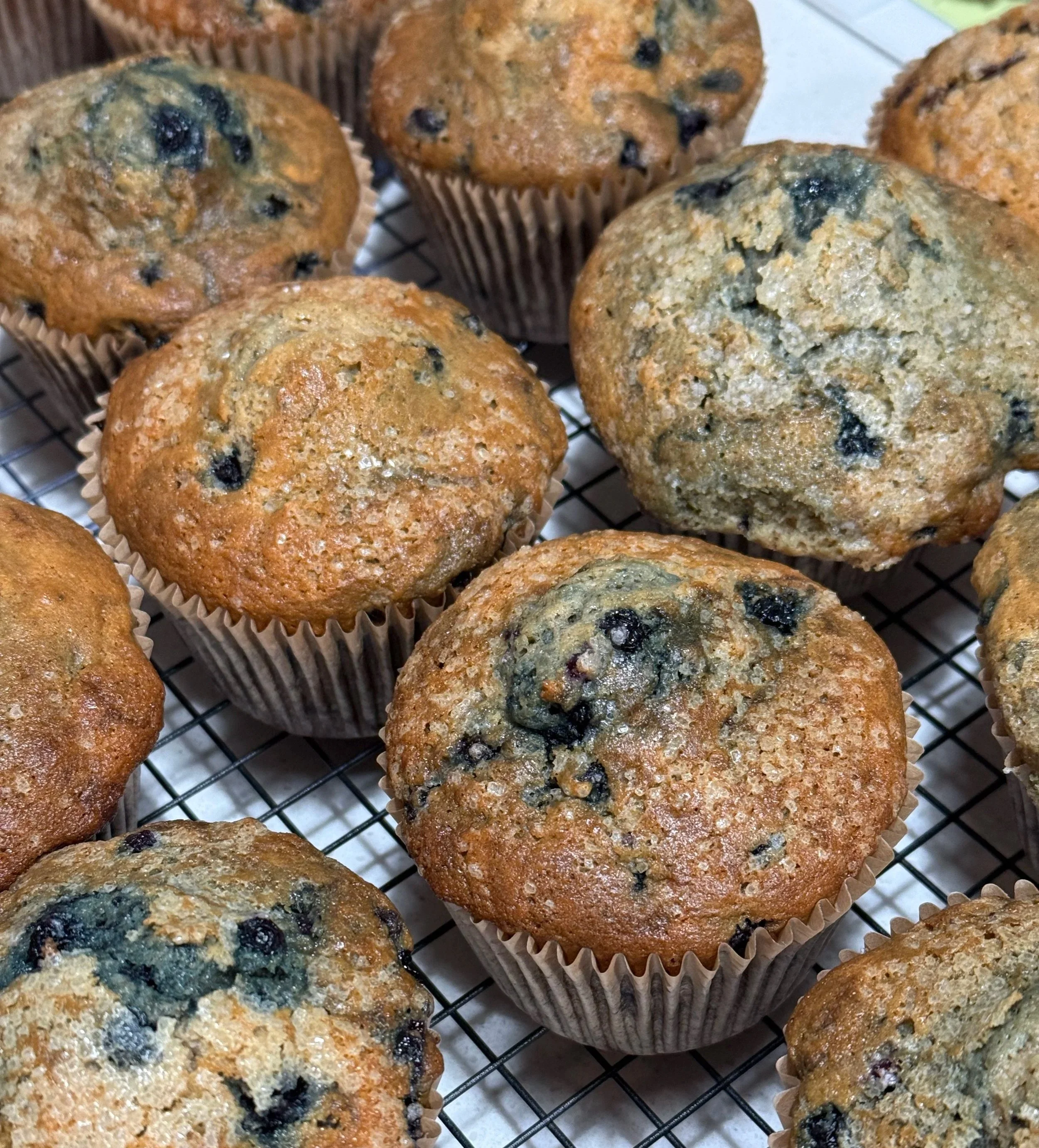 Freshly baked blueberry muffins cooling on a wire rack, with golden-brown tops and visible blueberries inside.