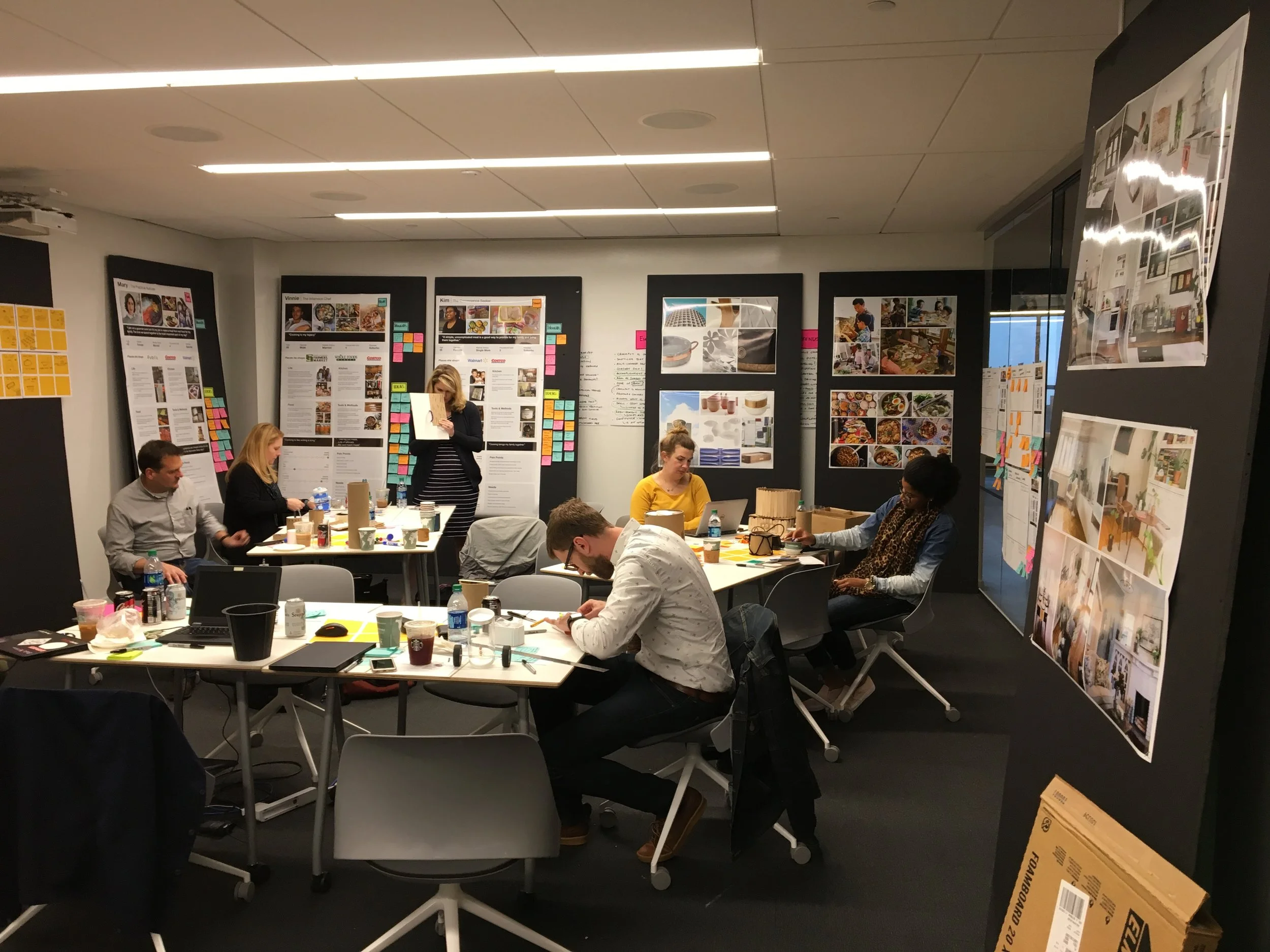 People working in a modern office space with boards covered in colorful sticky notes, papers, and images on the walls.